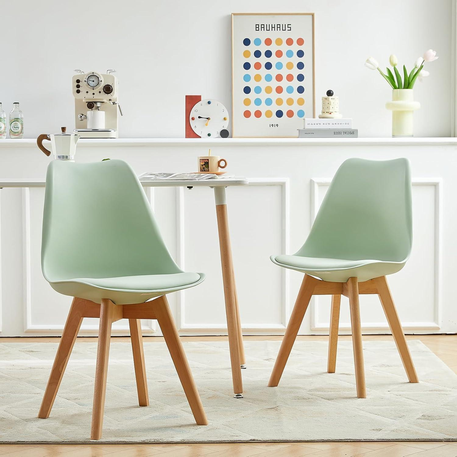 Due sedie verde chiaro con gambe in legno davanti a un piccolo tavolo in una stanza bianca.