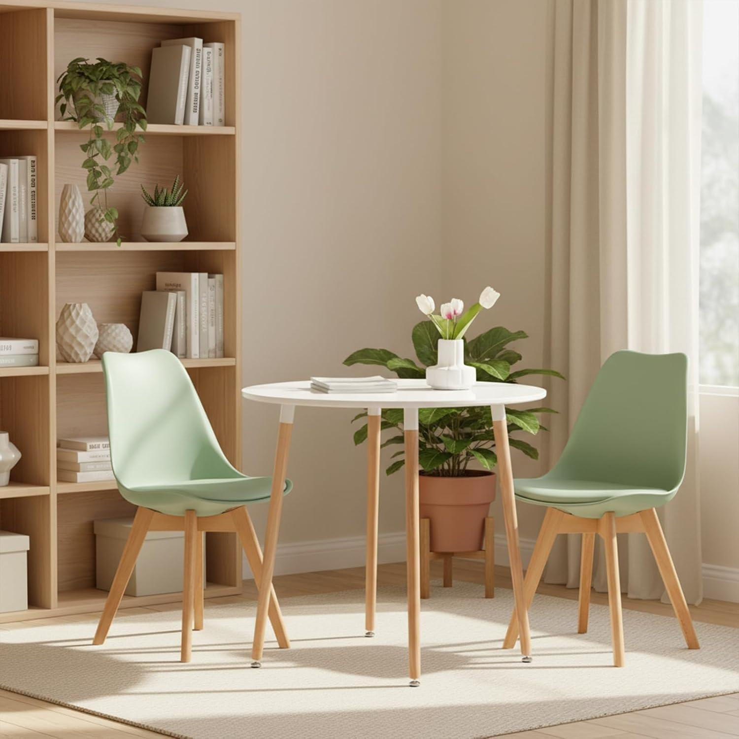 Un tavolo rotondo bianco con due sedie verdi, una pianta e una grande libreria in legno sullo sfondo.