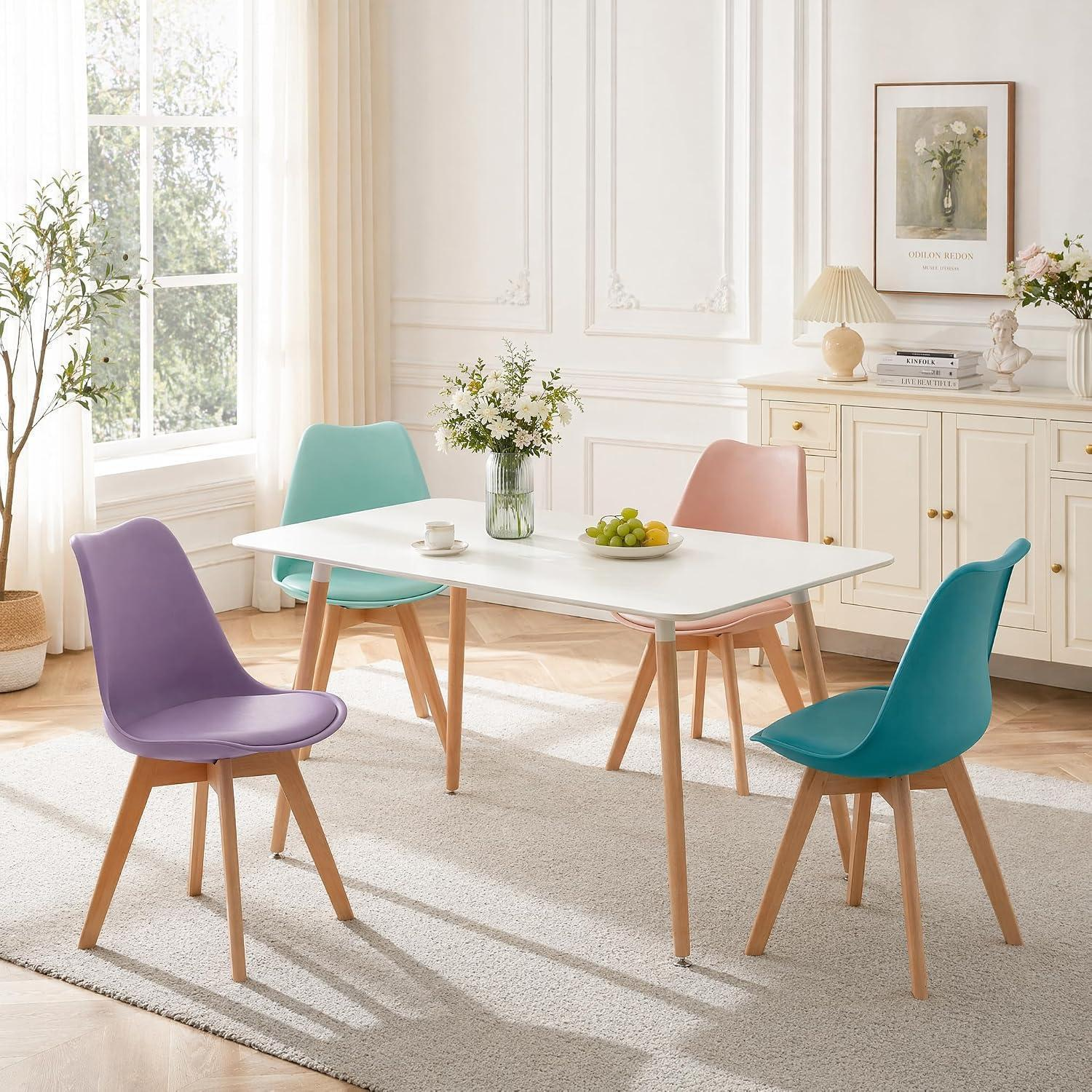 Una luminosa zona pranzo con tavolo bianco e quattro sedie colorate in viola, verde acqua, rosa e blu.