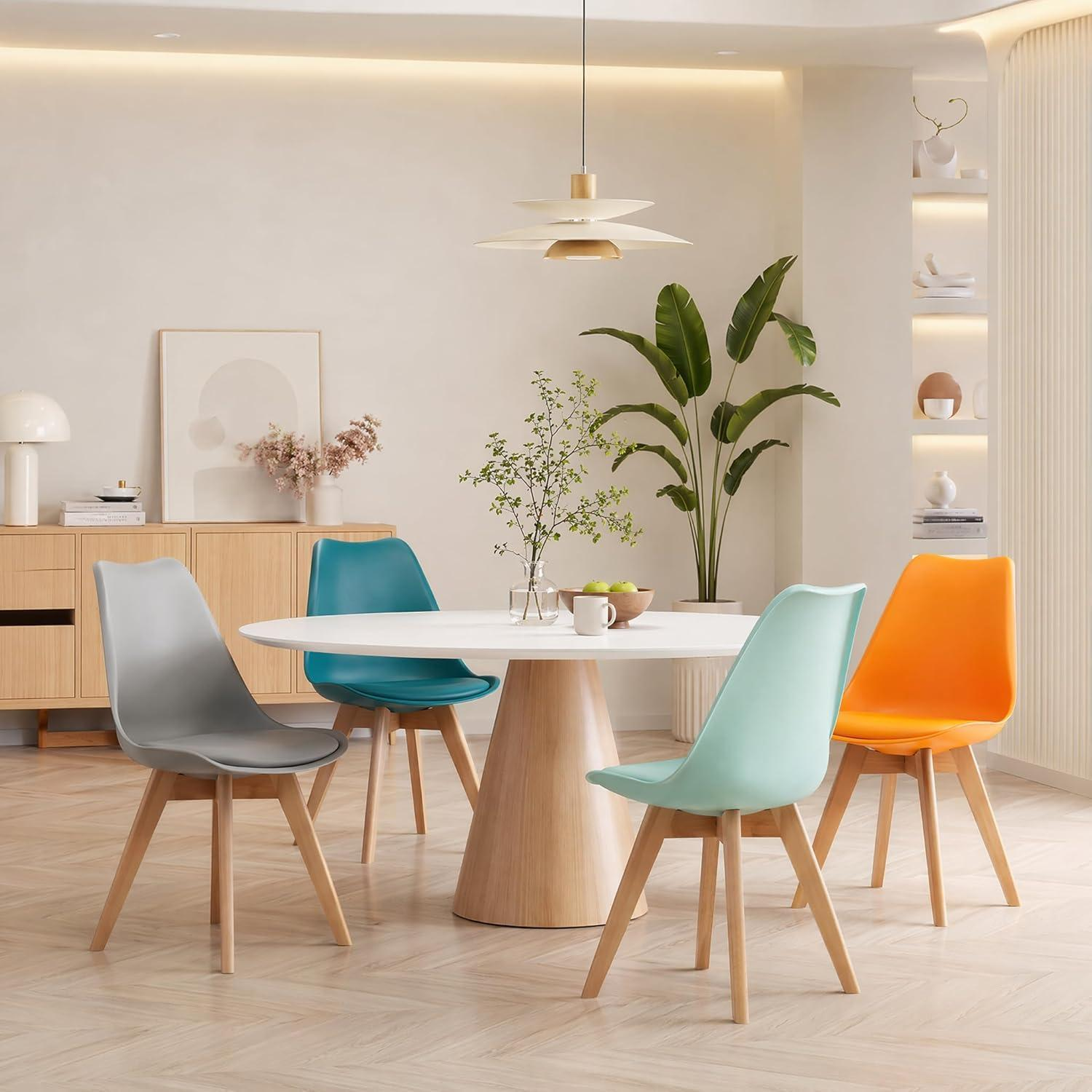 Moderno tavolo da pranzo con quattro sedie colorate, lampada a sospensione e piante in una stanza luminosa.