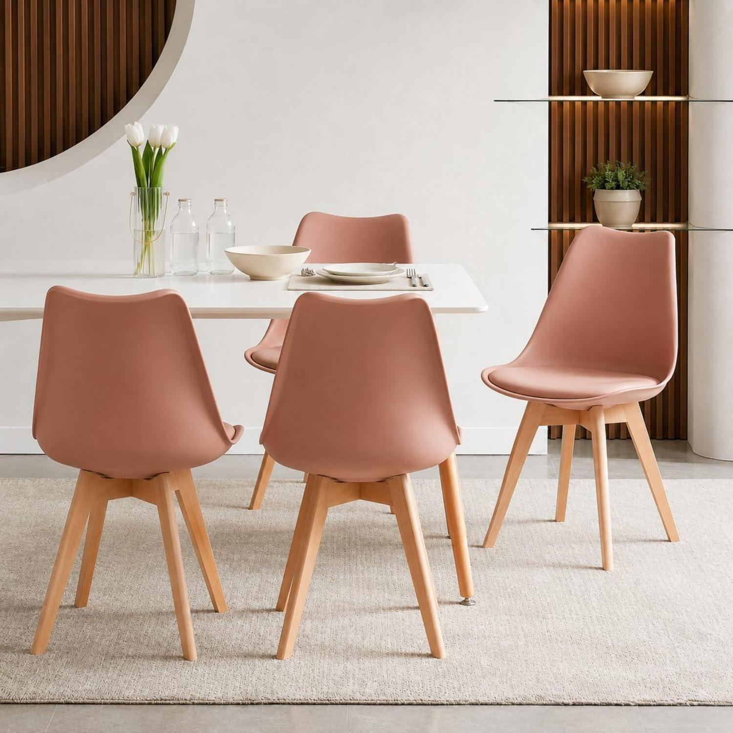 Sedie rosa moderne con gambe in legno attorno a un tavolo bianco in una stanza luminosa.