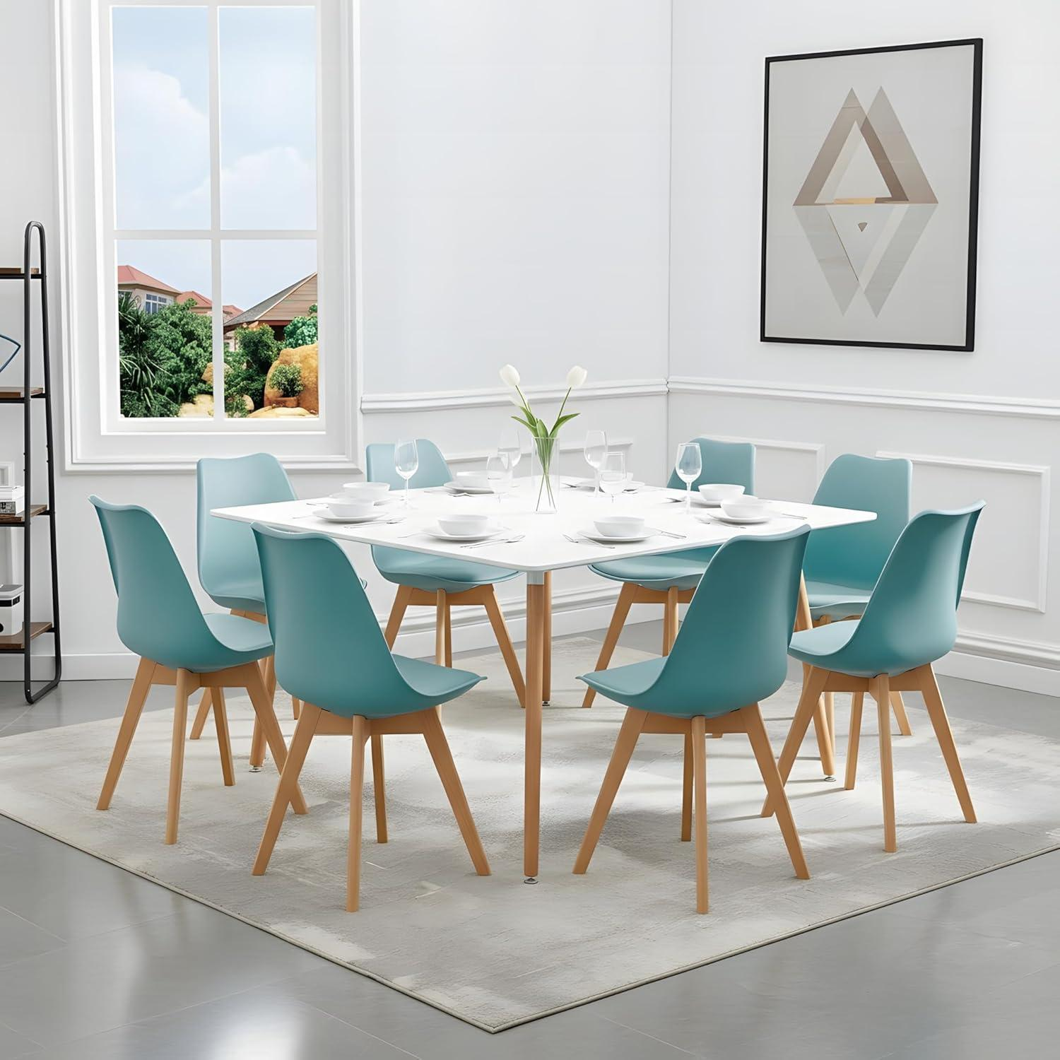 Un tavolo da pranzo bianco con sedie azzurre e gambe in legno in una stanza luminosa con una grande finestra.