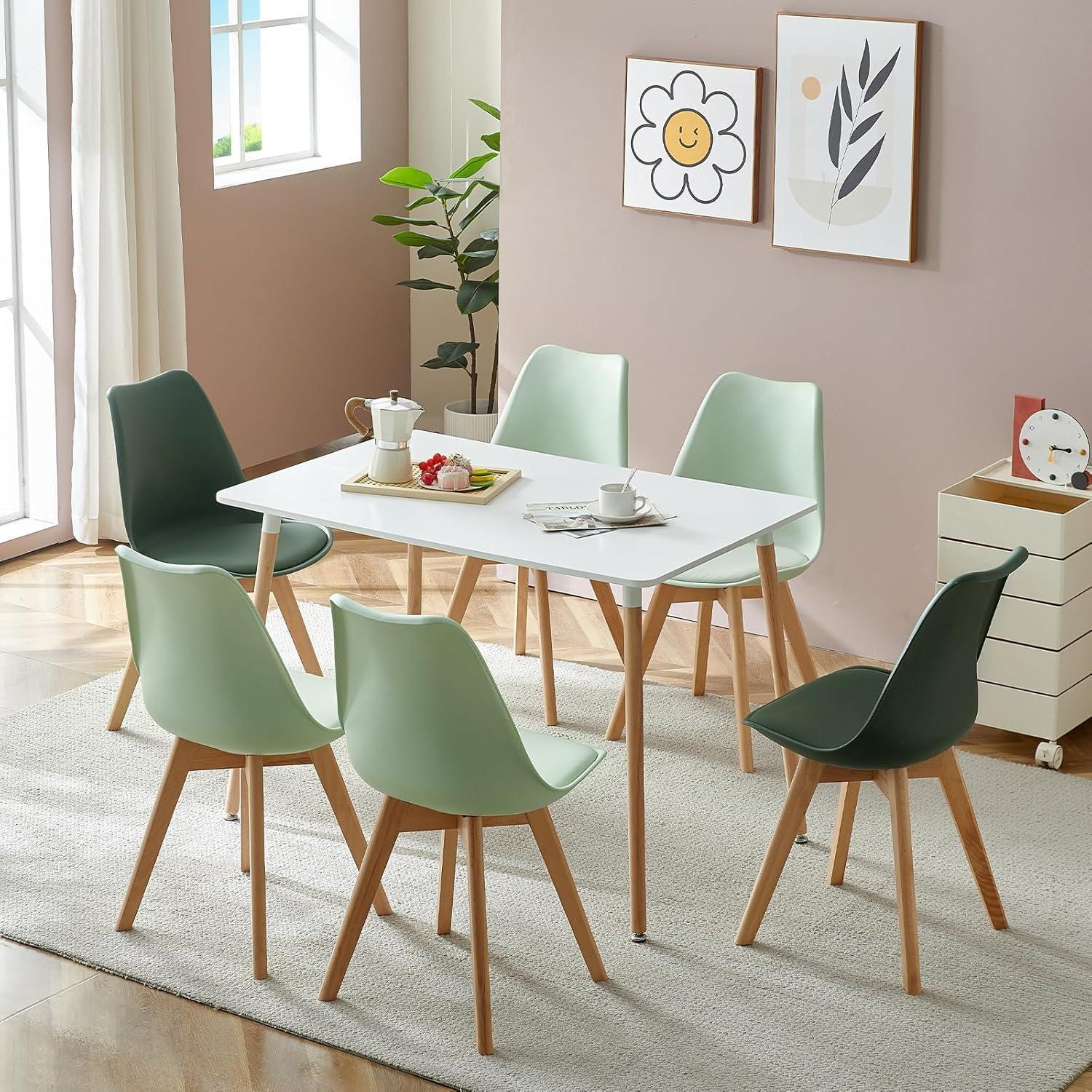 Un tavolo da pranzo bianco con sei sedie verde chiaro e scuro, posizionato su un tappeto in una stanza luminosa.