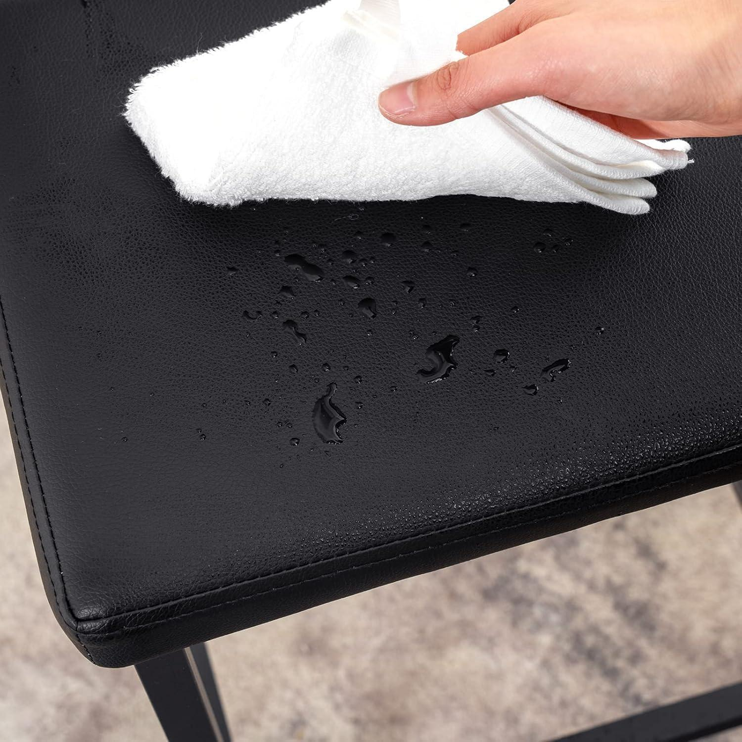 Una mano usa un panno bianco per asciugare le gocce d'acqua da una superficie di pelle nera.