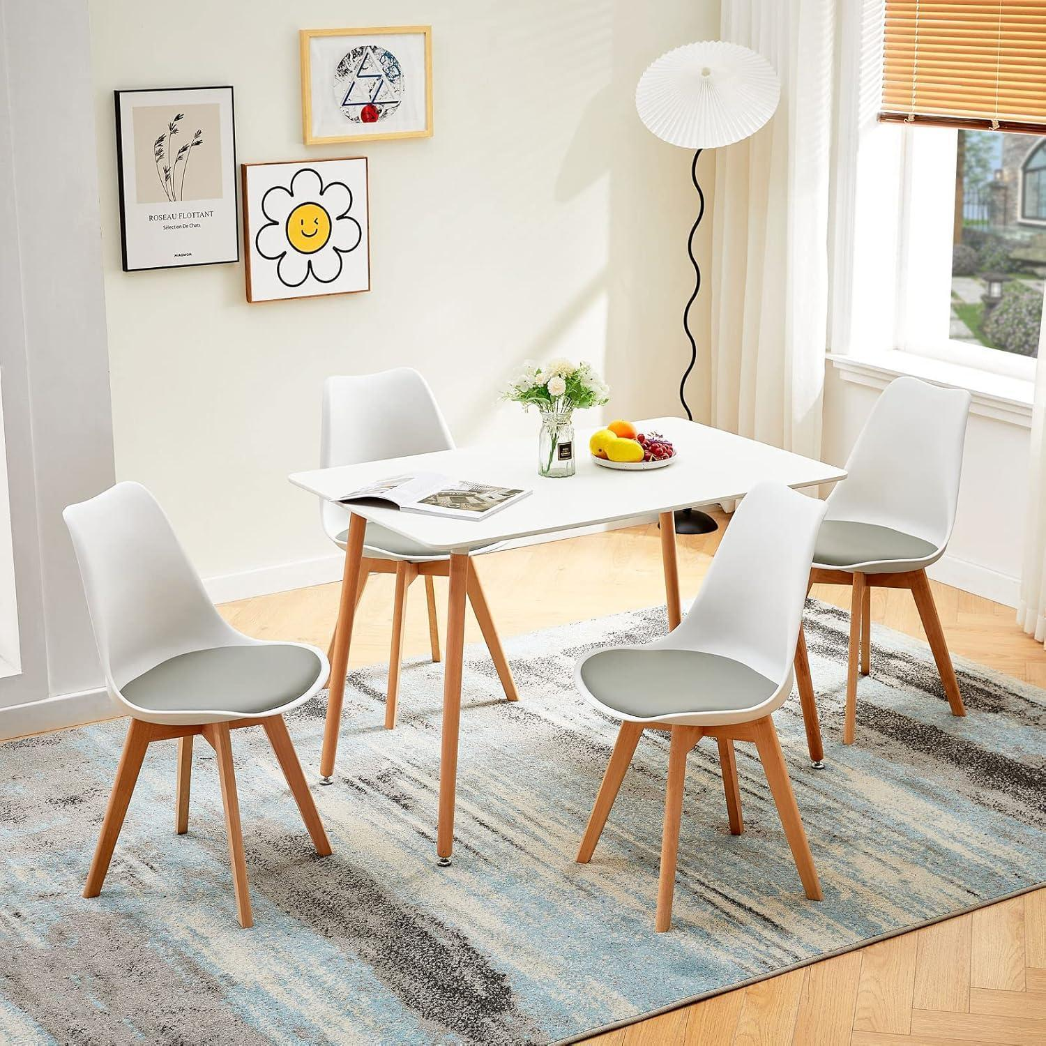 Moderno tavolo da pranzo con quattro sedie bianche su un tappeto blu-grigio in una stanza luminosa.