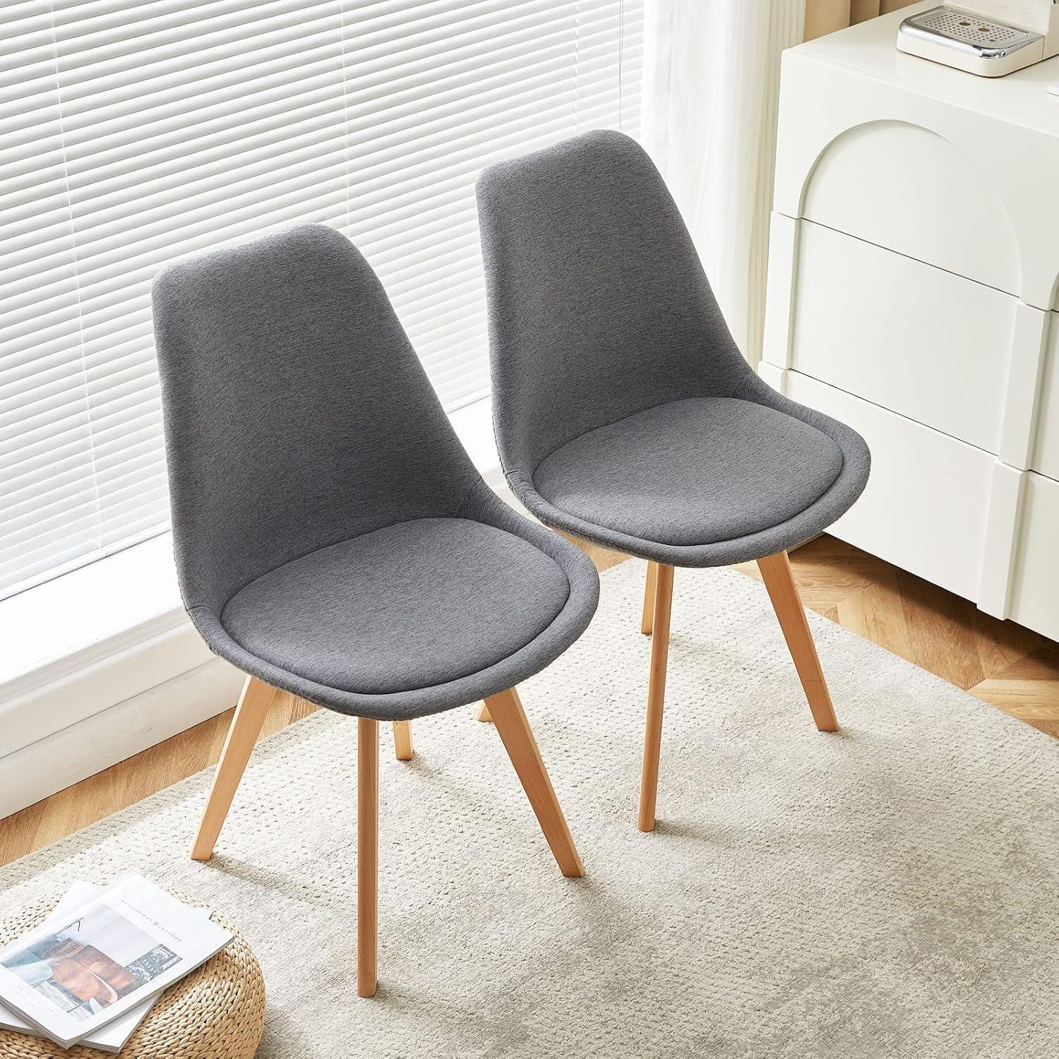 Due sedie grigie con gambe in legno su un tappeto davanti alle tende.