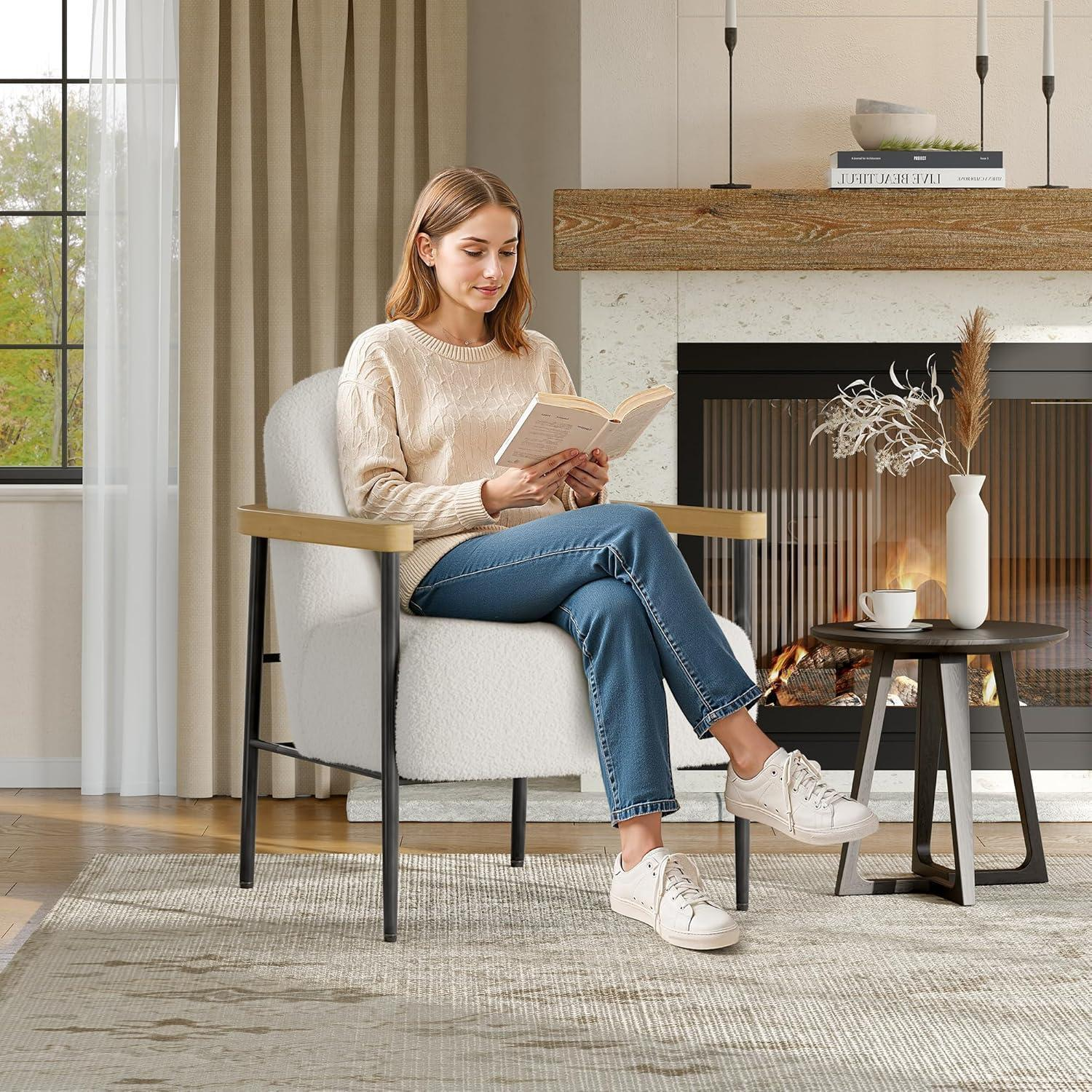 Una donna in jeans e maglione legge un libro in una poltrona bianca vicino a un caminetto.