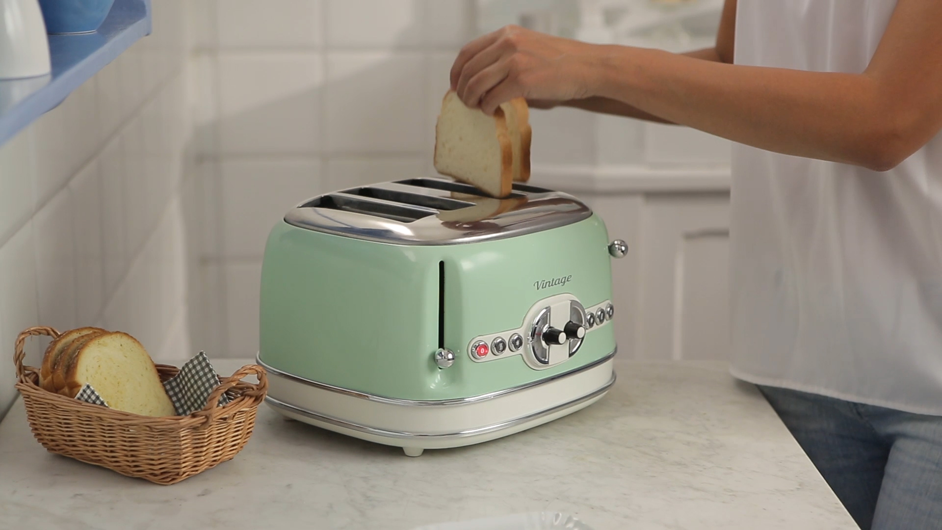 Eine Person legt Brotscheiben in einen mintgrünen Vintage-Toaster auf einer Küchentheke.