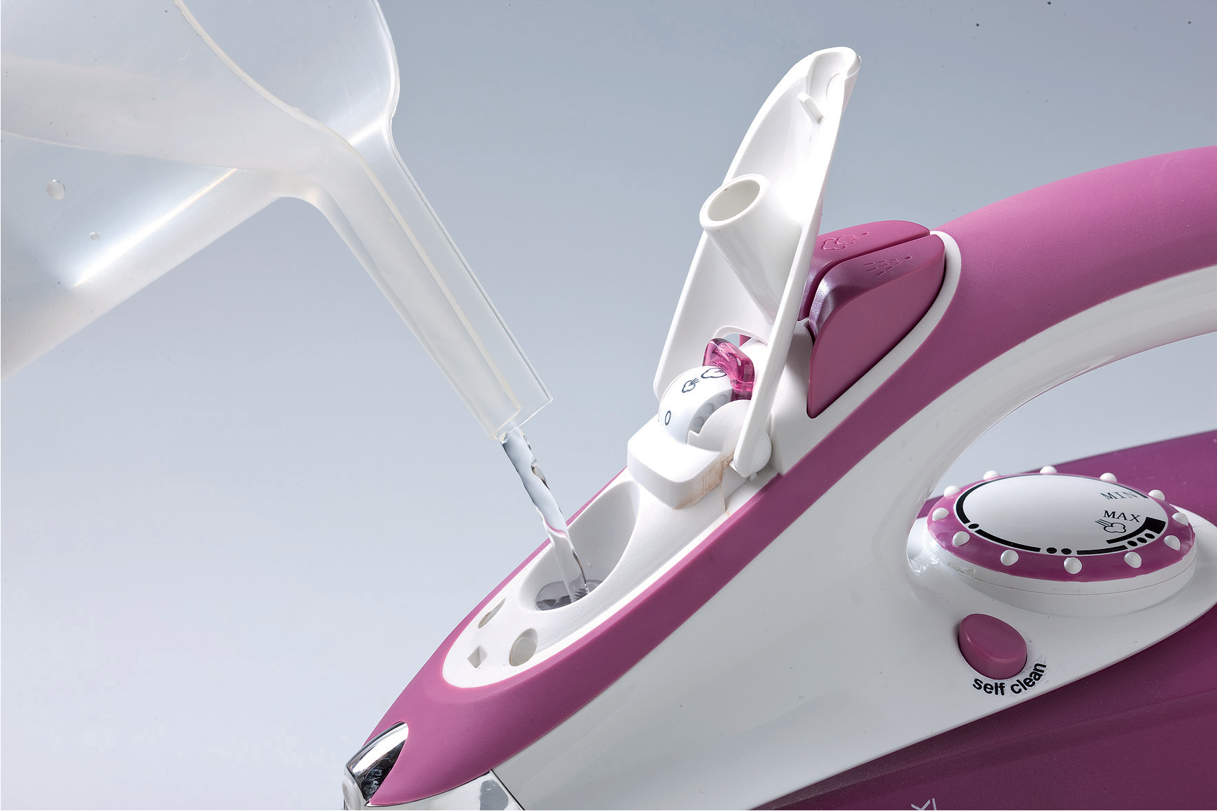 Wasser wird aus einem Messbecher in den Wassertank eines pink-weißen Bügeleisens gefüllt.