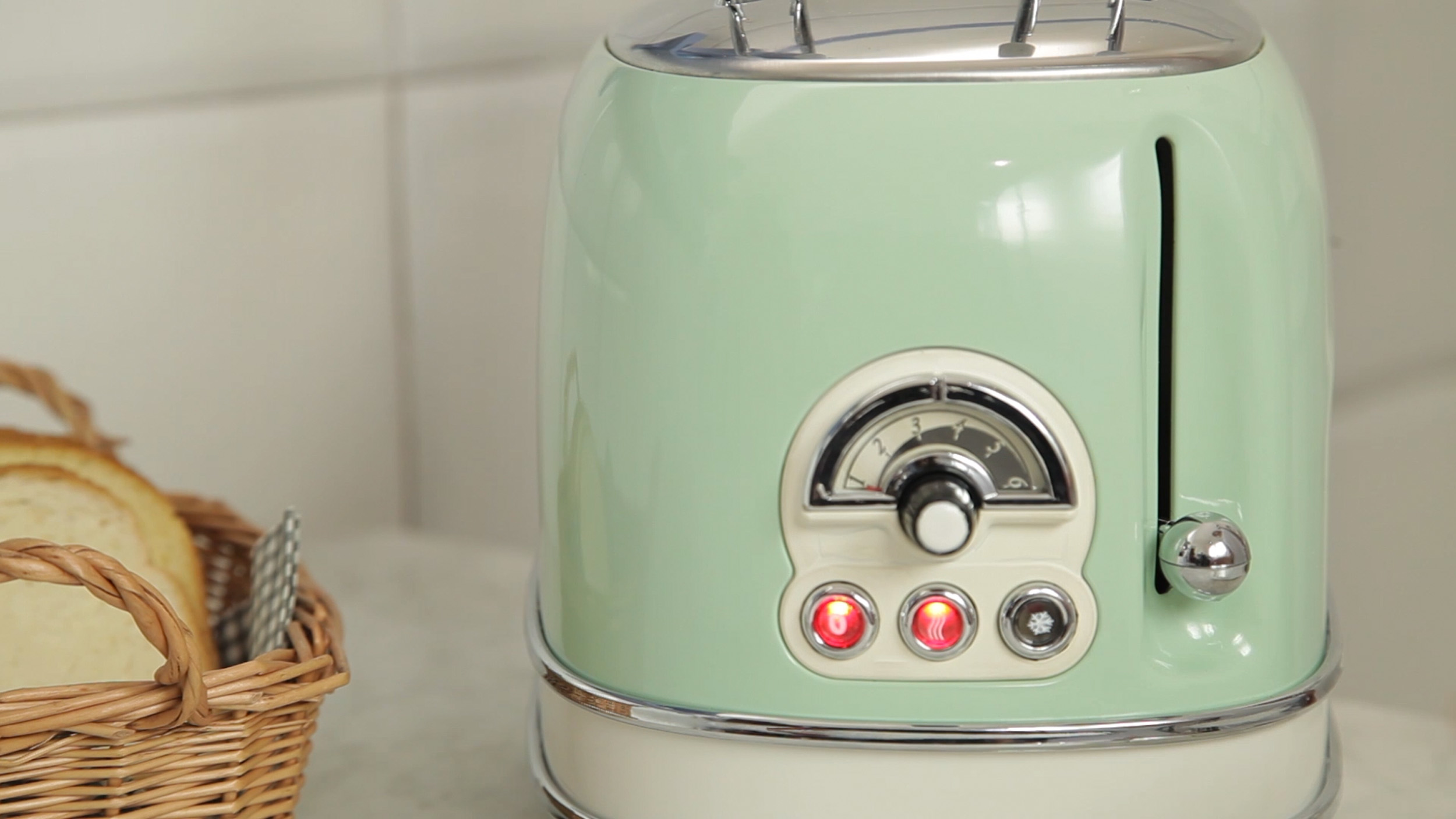 Ein pastellgrüner Retro-Toaster auf einer Arbeitsplatte neben einem Brotkorb in einer Küche.
