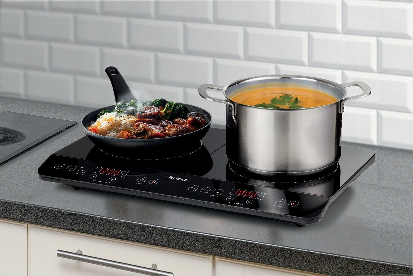 A black induction cooktop with a pan of meat and vegetables and a pot of soup.