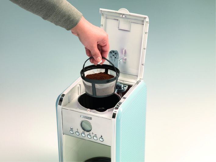 A hand places a filled coffee filter into a light blue drip coffee maker.