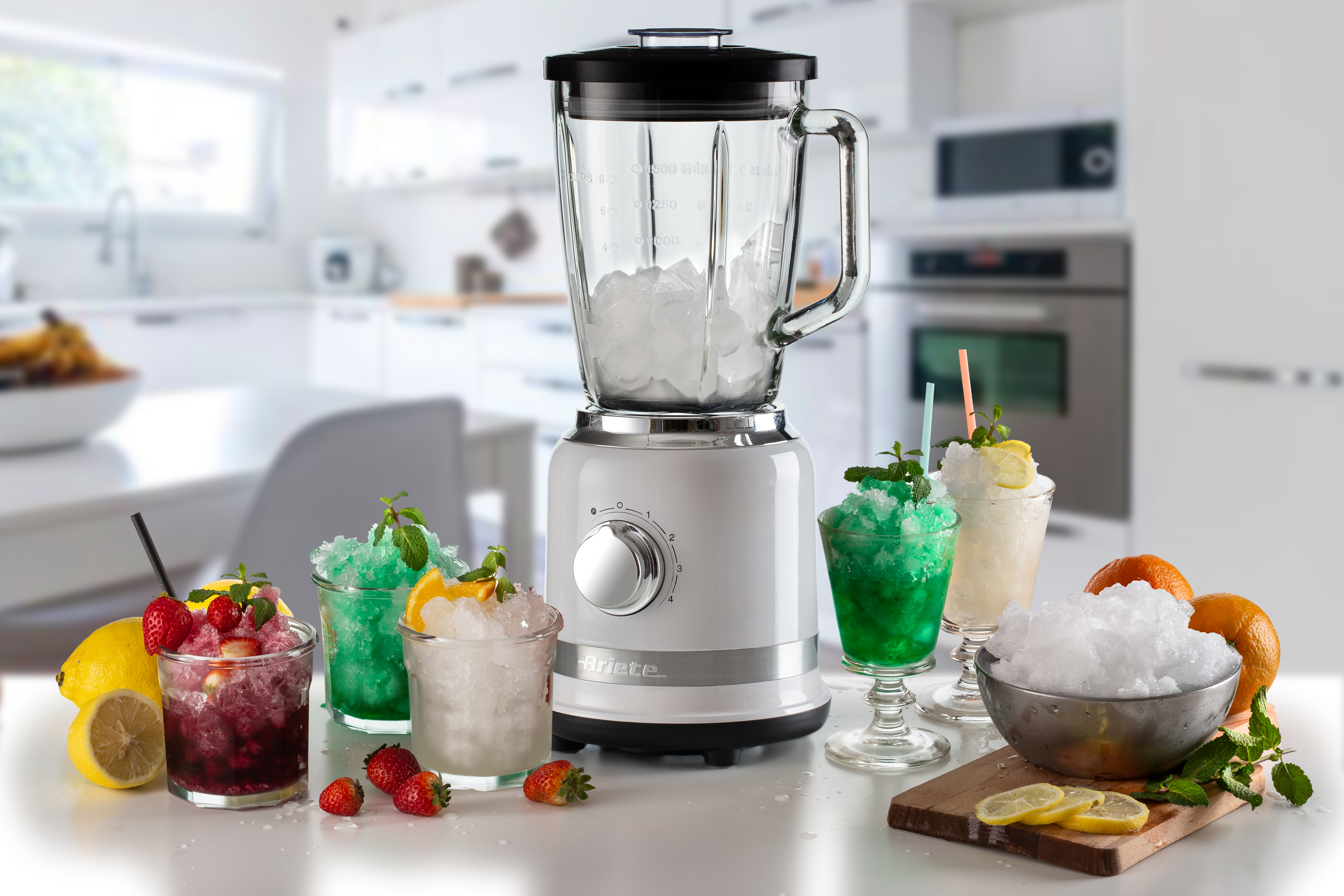 Beyaz bir blender mutfak tezgahında duruyor, etrafında renkli buzlu içecekler, meyveler ve buz var.