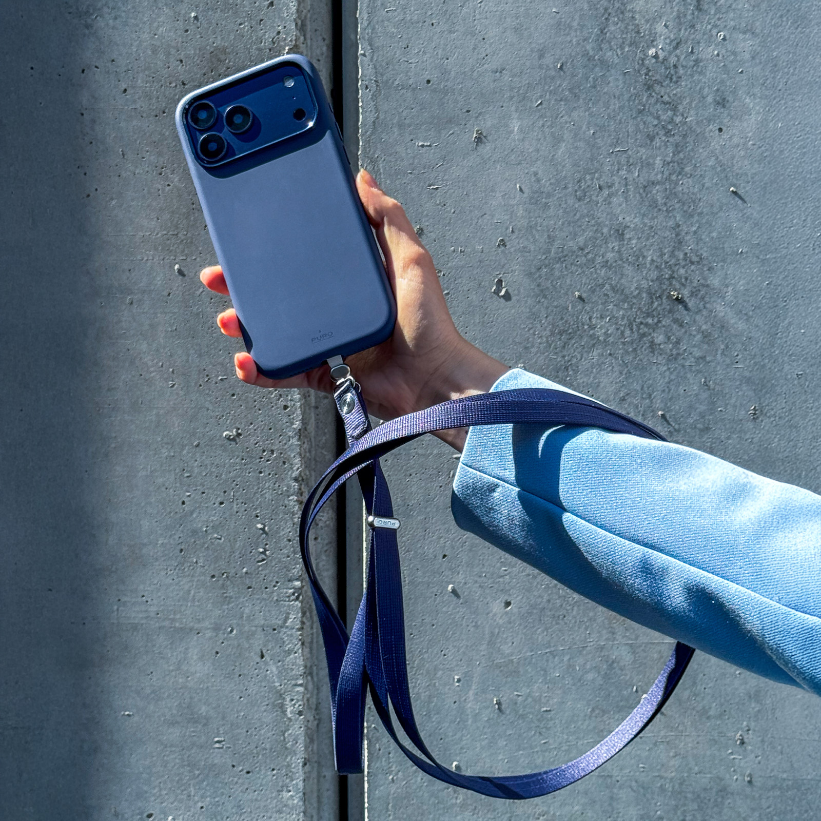 Una mano sosteniendo un smartphone azul con correa a juego contra un muro de hormigón.