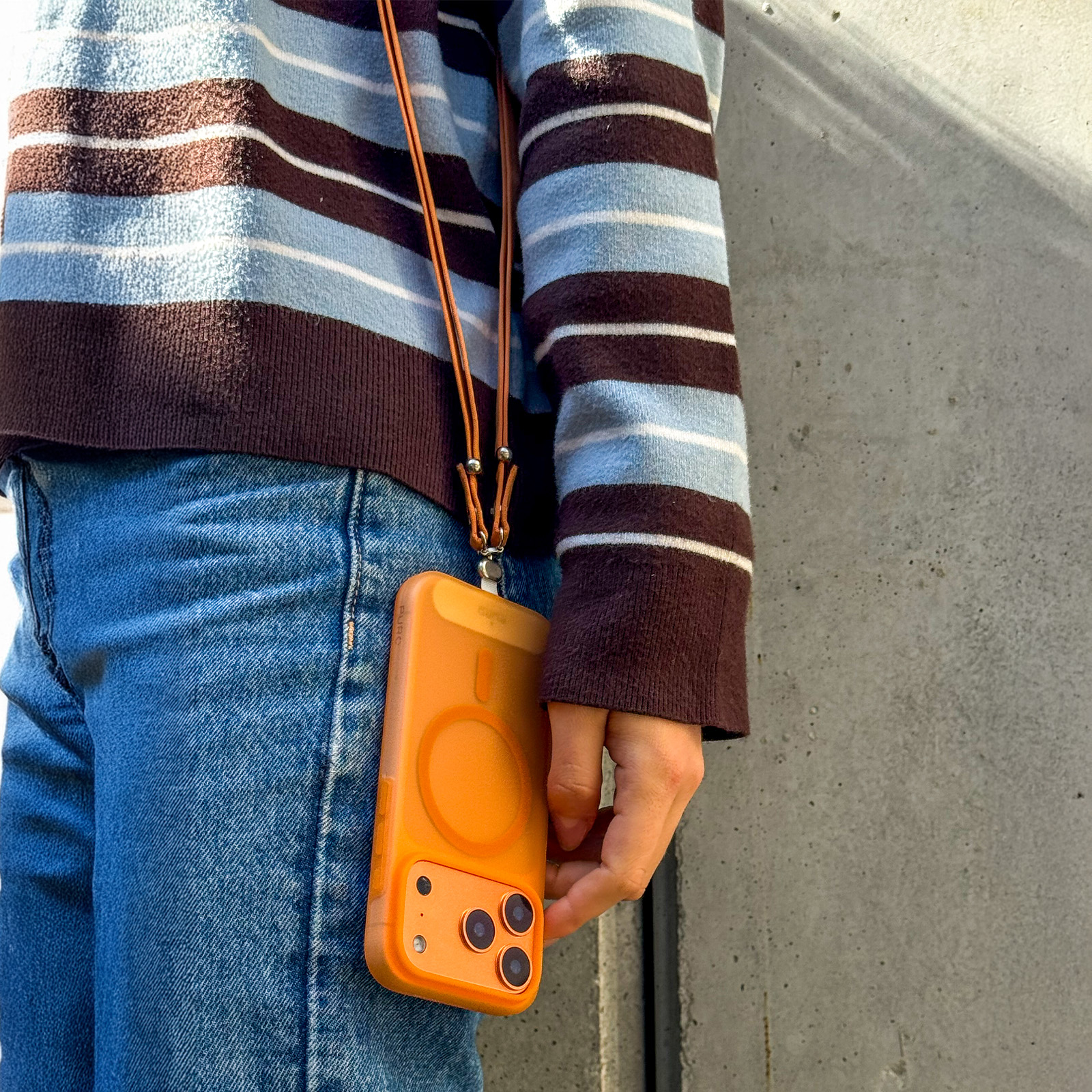Persona con suéter de rayas azules y marrones usando una funda de teléfono naranja con correa.