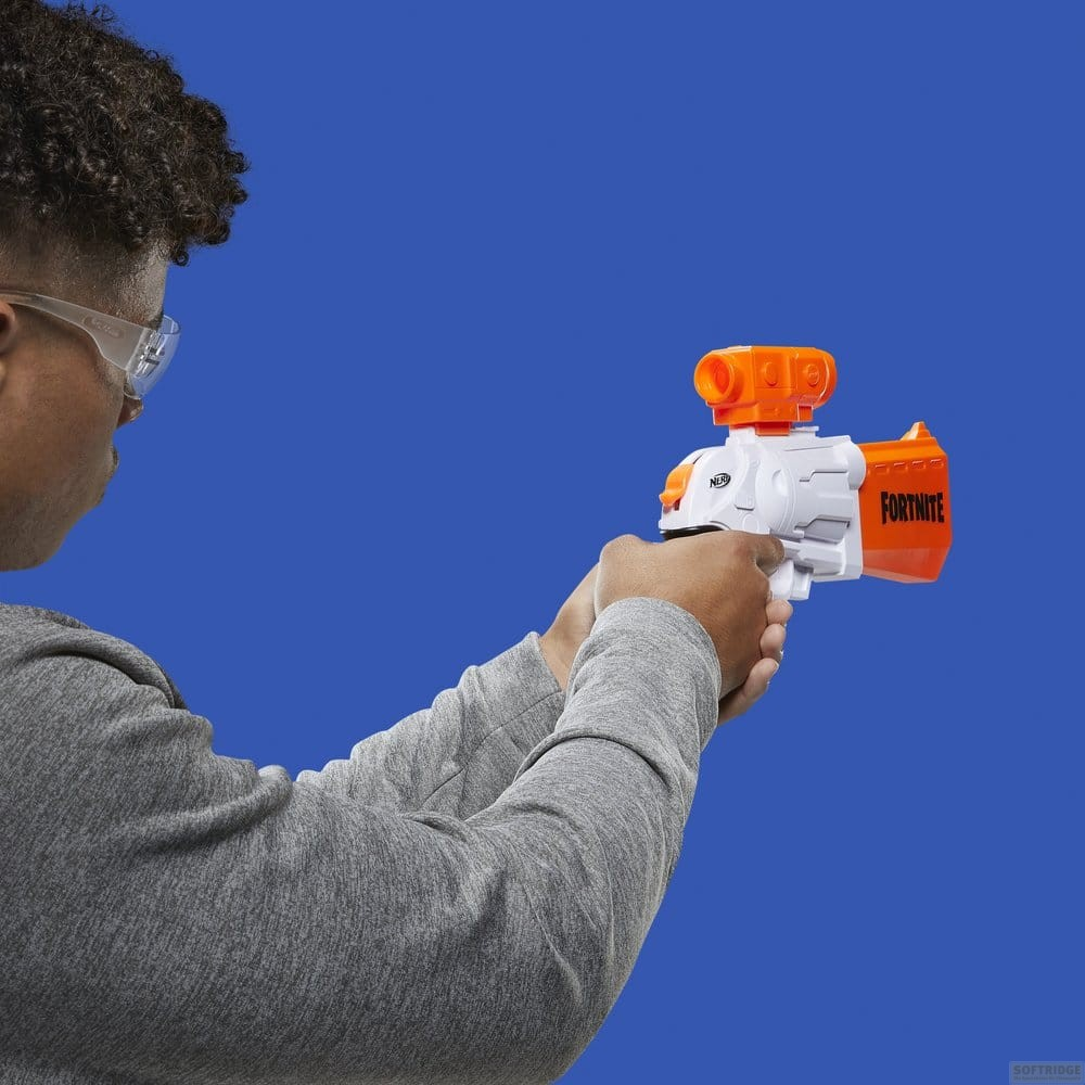 Ein Junge in einem grauen Pullover zielt mit einem orange-weißen Fortnite Nerf-Blaster vor blauem Hintergrund.