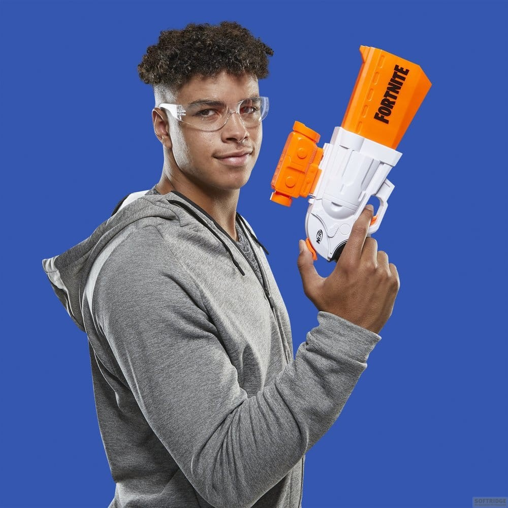 Ein junger Mann mit Brille und grauer Kapuzenjacke hält eine orangeweiße Fortnite Nerf-Gun vor blauem Hintergrund.