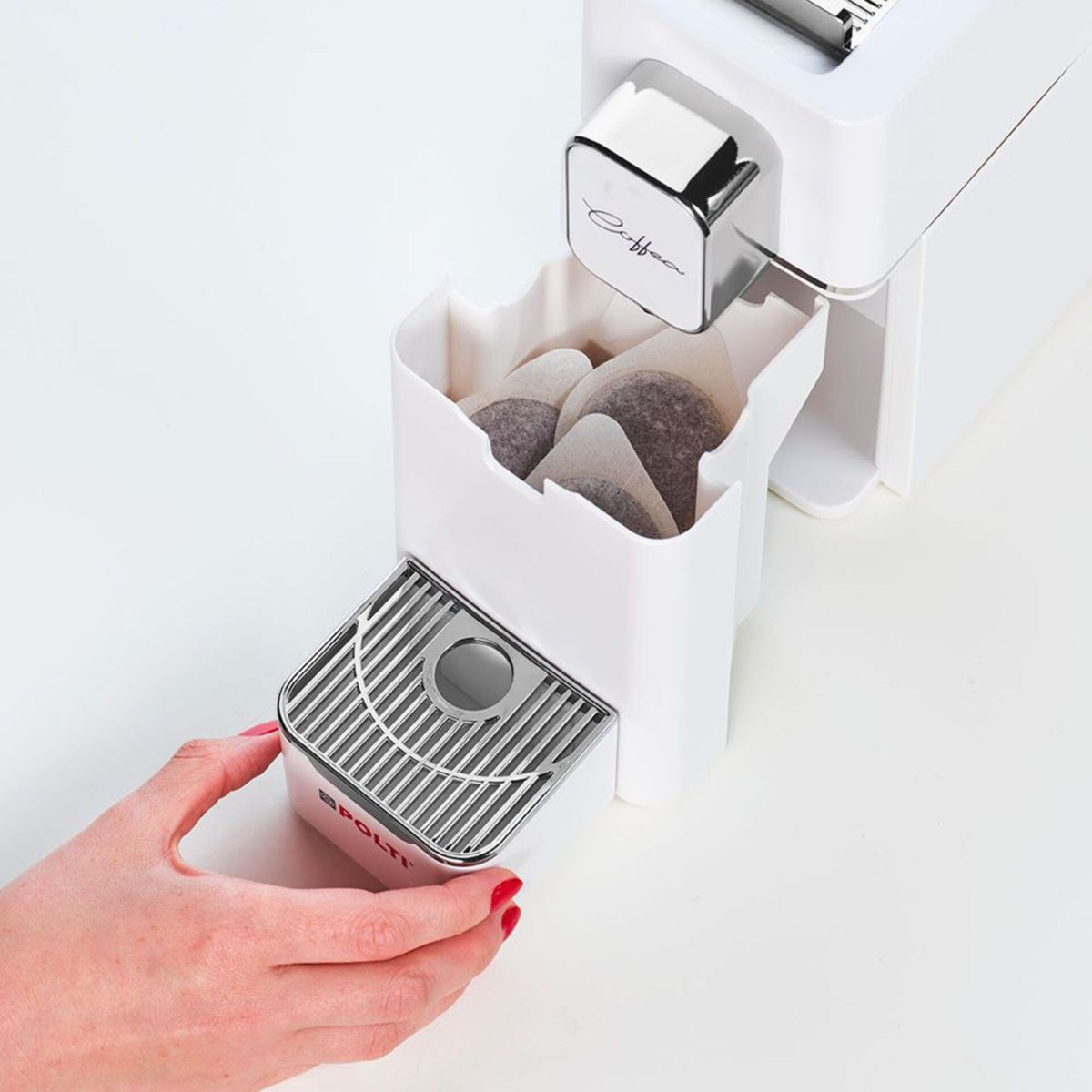 Eine Hand öffnet den Behälter einer weißen Kaffeemaschine mit Kaffeepads.
