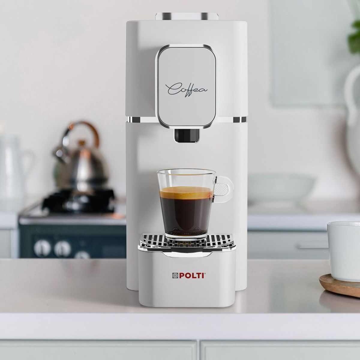 Eine weiße Polti-Kaffeemaschine auf einer Theke mit einer Glastasse Espresso vor einer Küche.
