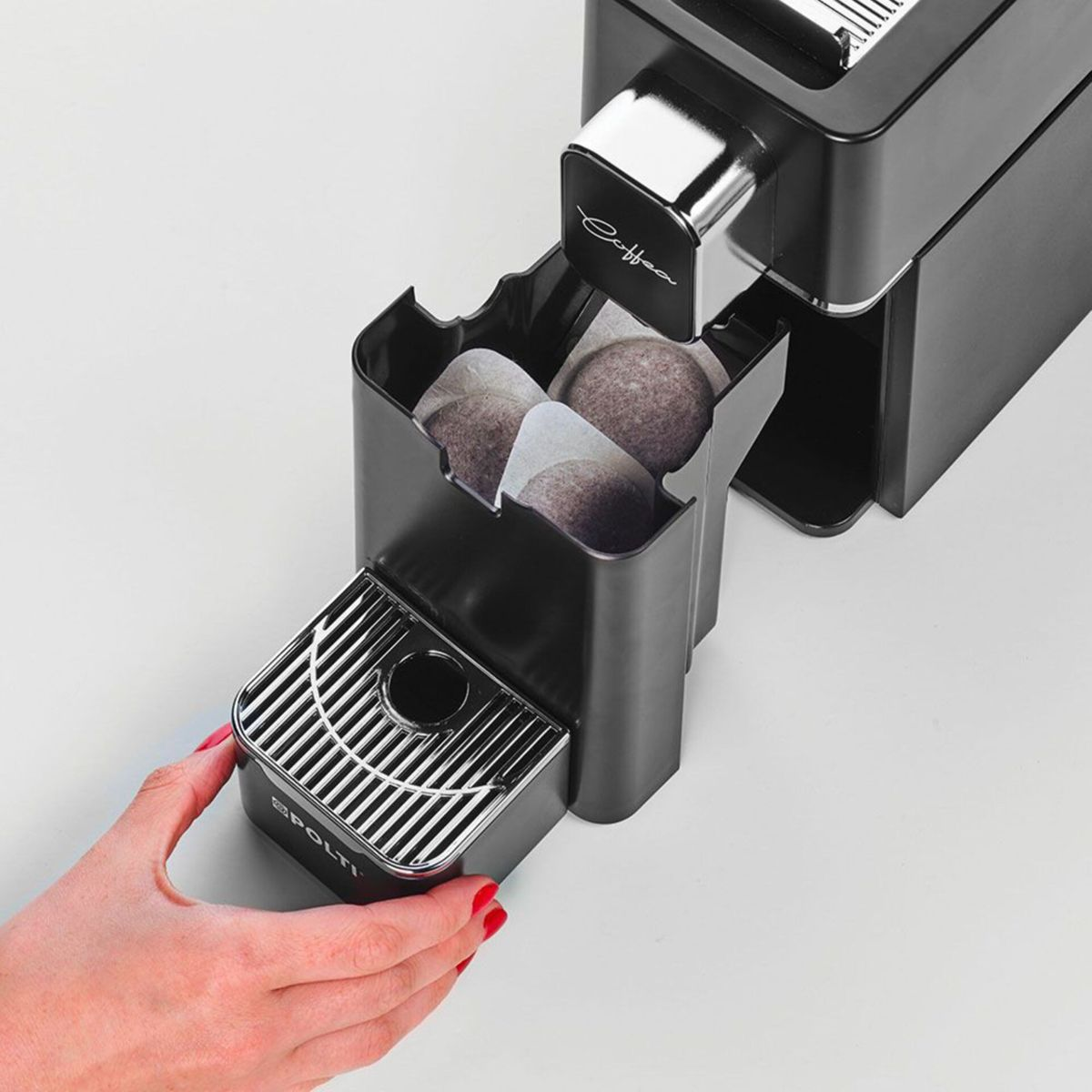 Eine Hand zieht das Fach einer schwarzen Kaffeemaschine heraus, in dem Kaffeepads liegen.
