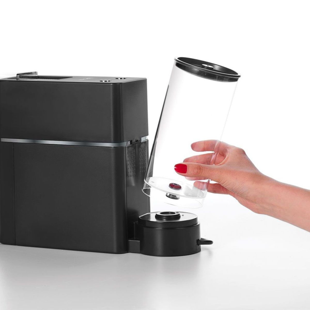 Eine Hand mit rotem Nagellack setzt einen transparenten Wassertank in eine schwarze Kaffeemaschine ein.