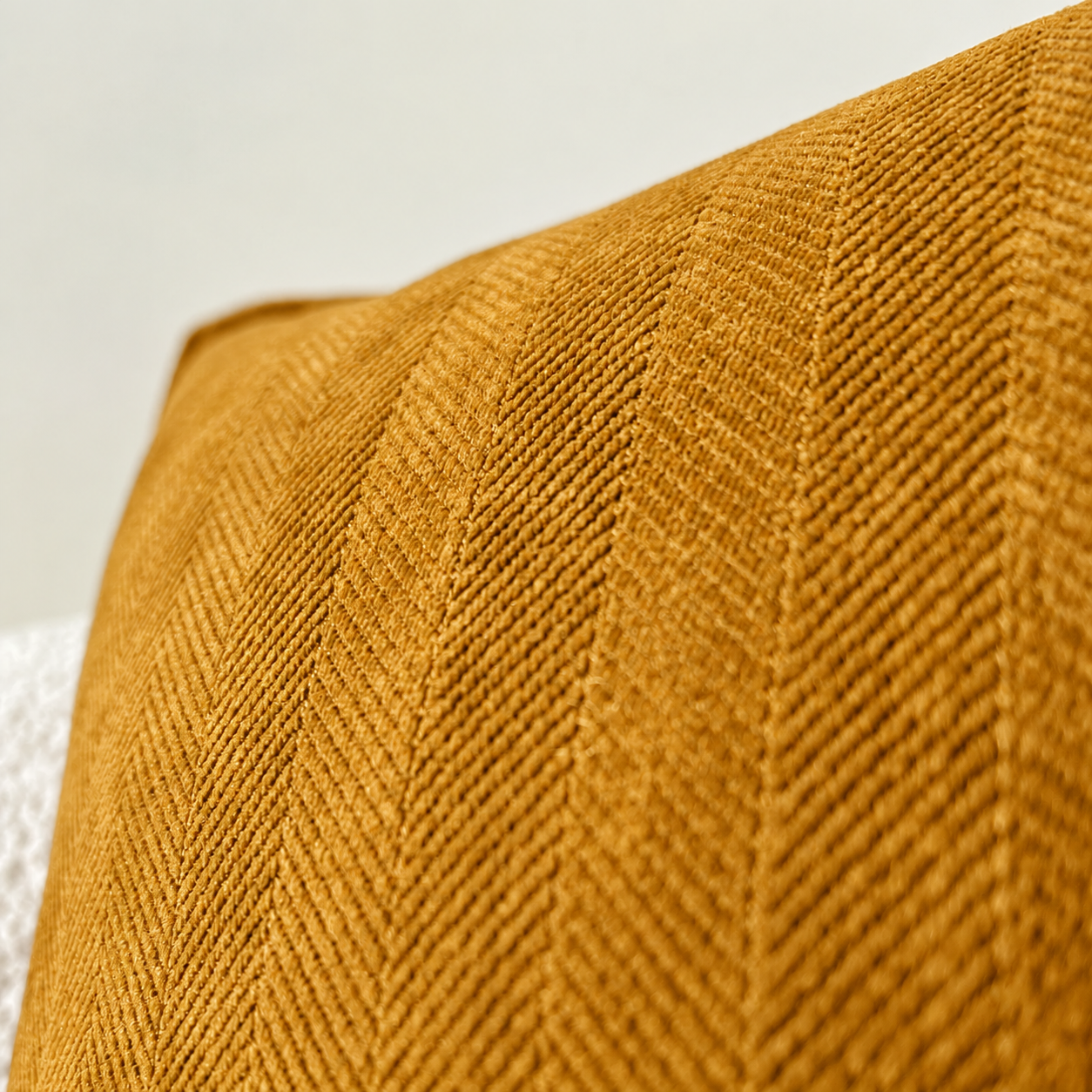 Nahaufnahme eines goldenen Kissens mit Chevron-Muster vor weißem Hintergrund.