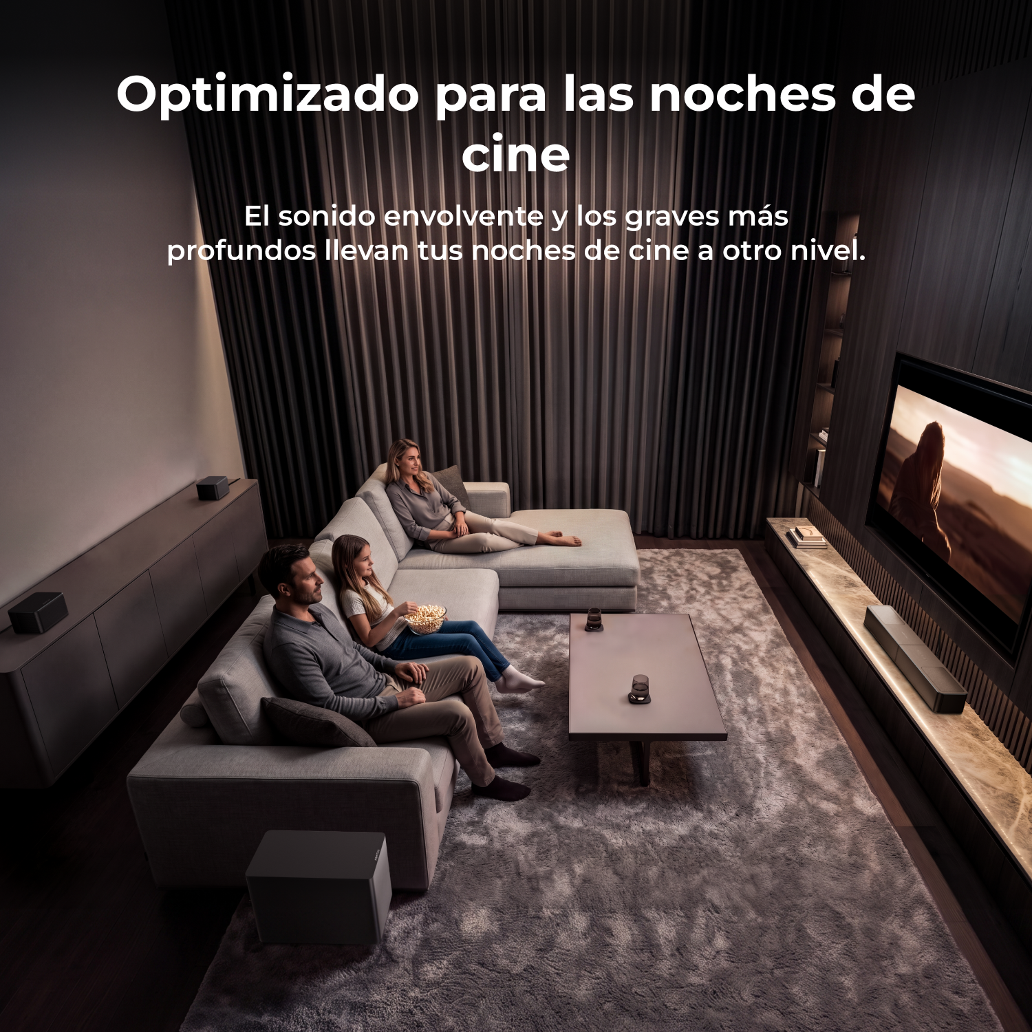 Una familia se sienta cómodamente en un sofá viendo una película en una sala tenuemente iluminada.