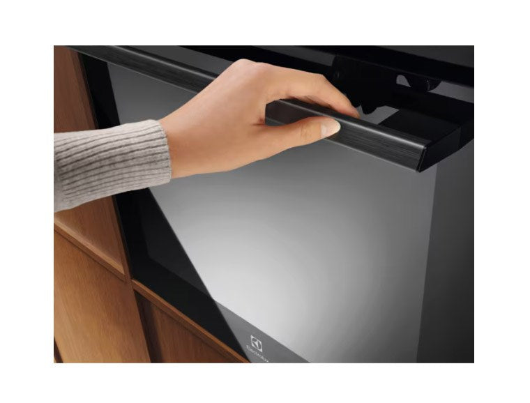 Una mano afferra la maniglia nera di un forno moderno inserito in mobili in legno.