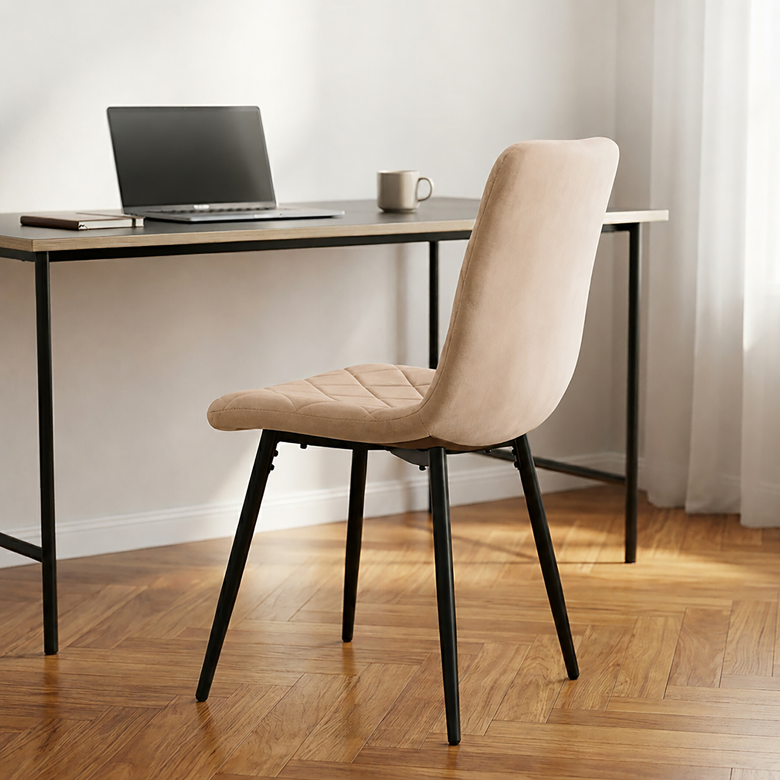 Ein beige getufteter Stuhl vor einem modernen Schreibtisch mit Laptop, Notizbuch und Tasse.