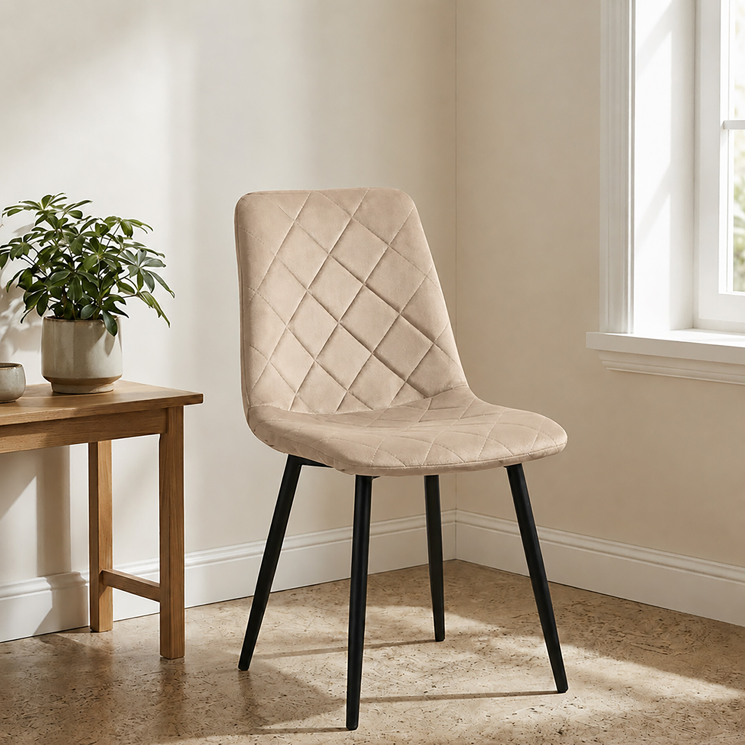 Ein beige gesteppter Stuhl mit schwarzen Beinen steht in einem hellen Zimmer neben einer Pflanze.