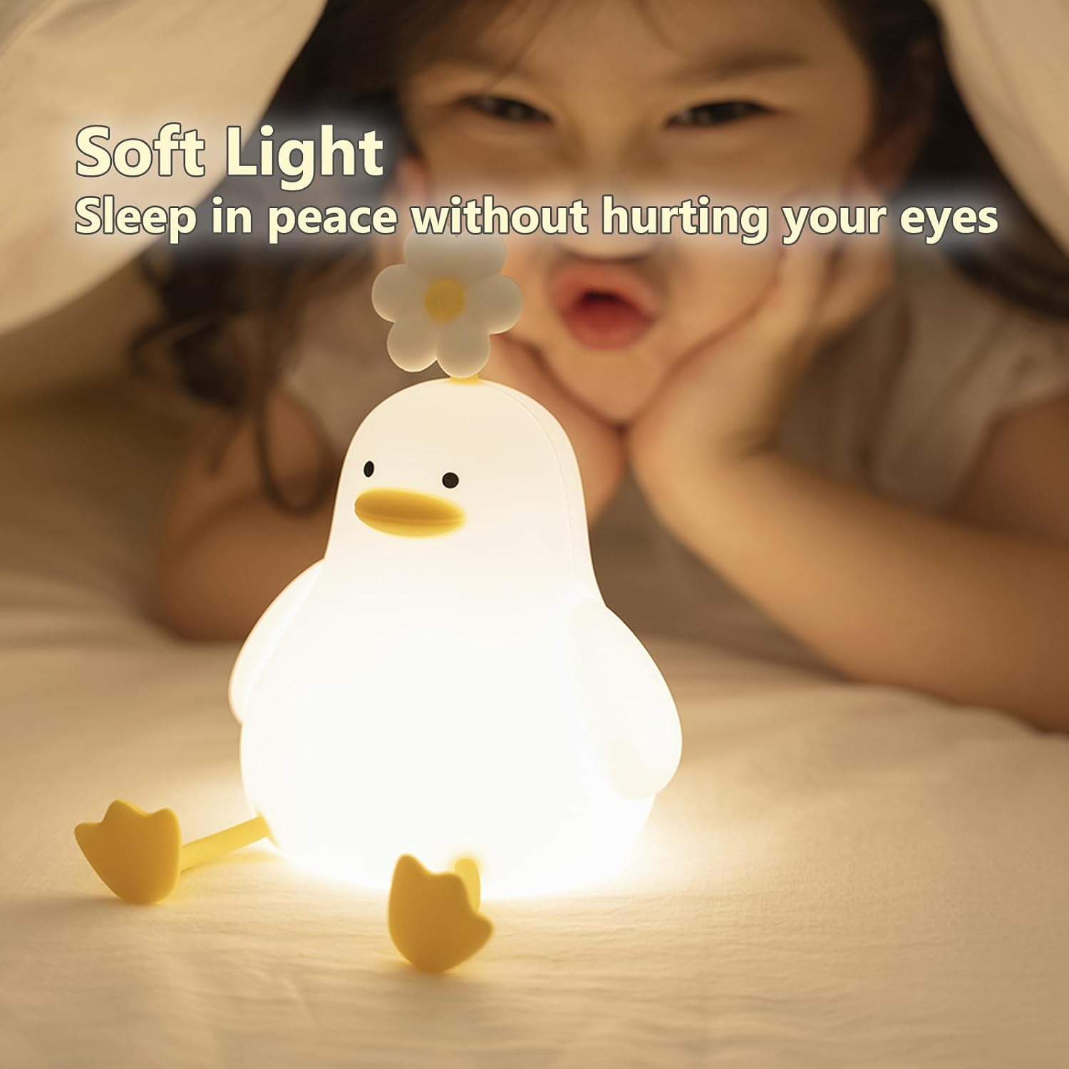 Eine süße, leuchtende Entenlampe mit einer Blume sitzt auf einem Bett, während ein Mädchen im Hintergrund zuschaut.