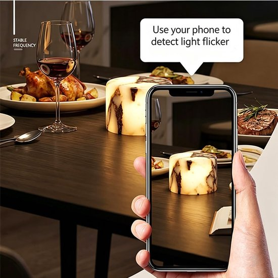 Eine Hand hält ein Smartphone, das ein beleuchtetes Objekt auf einem Esstisch filmt.