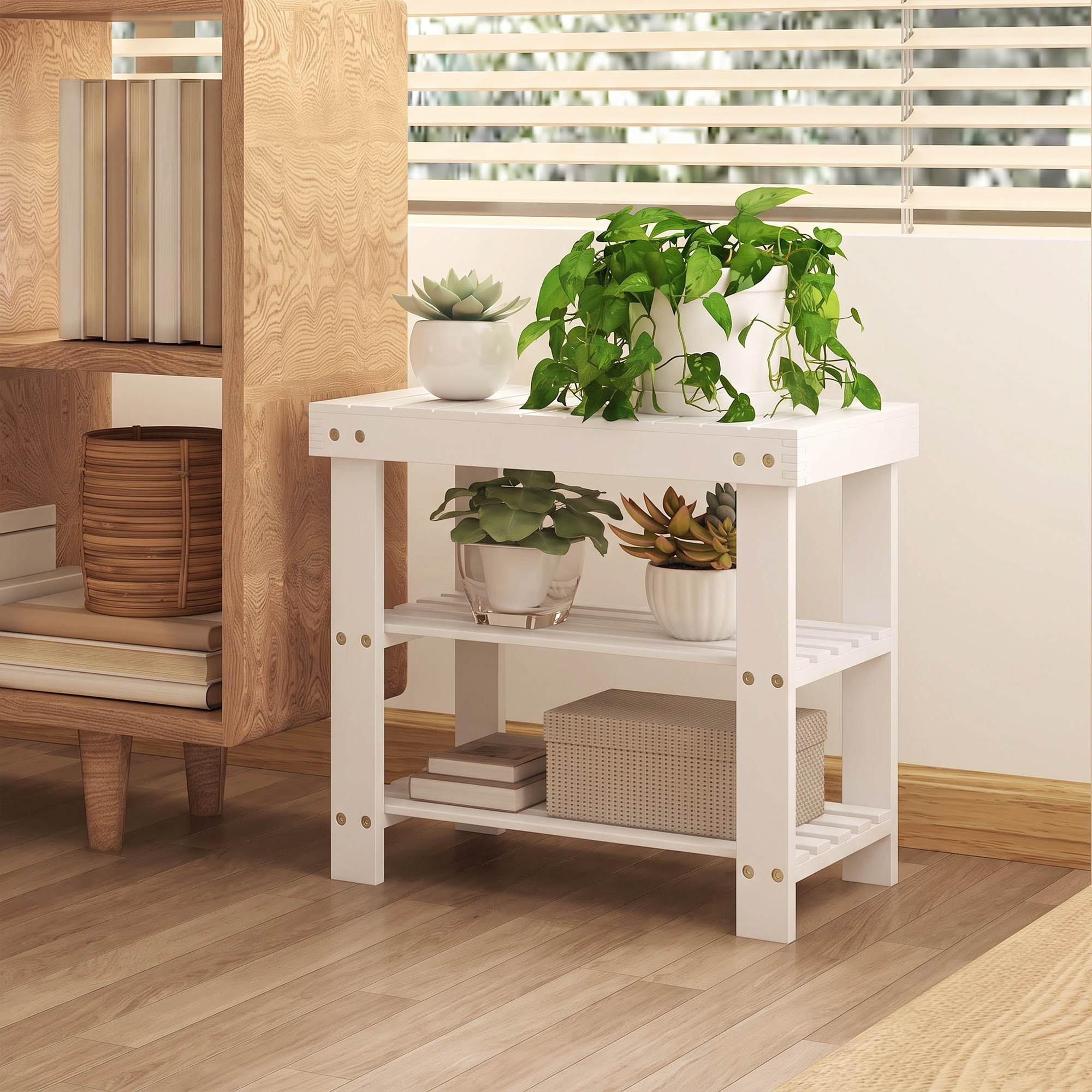 Una estantería de madera blanca con plantas en maceta y una caja está al lado de un mueble de madera frente a una ventana.