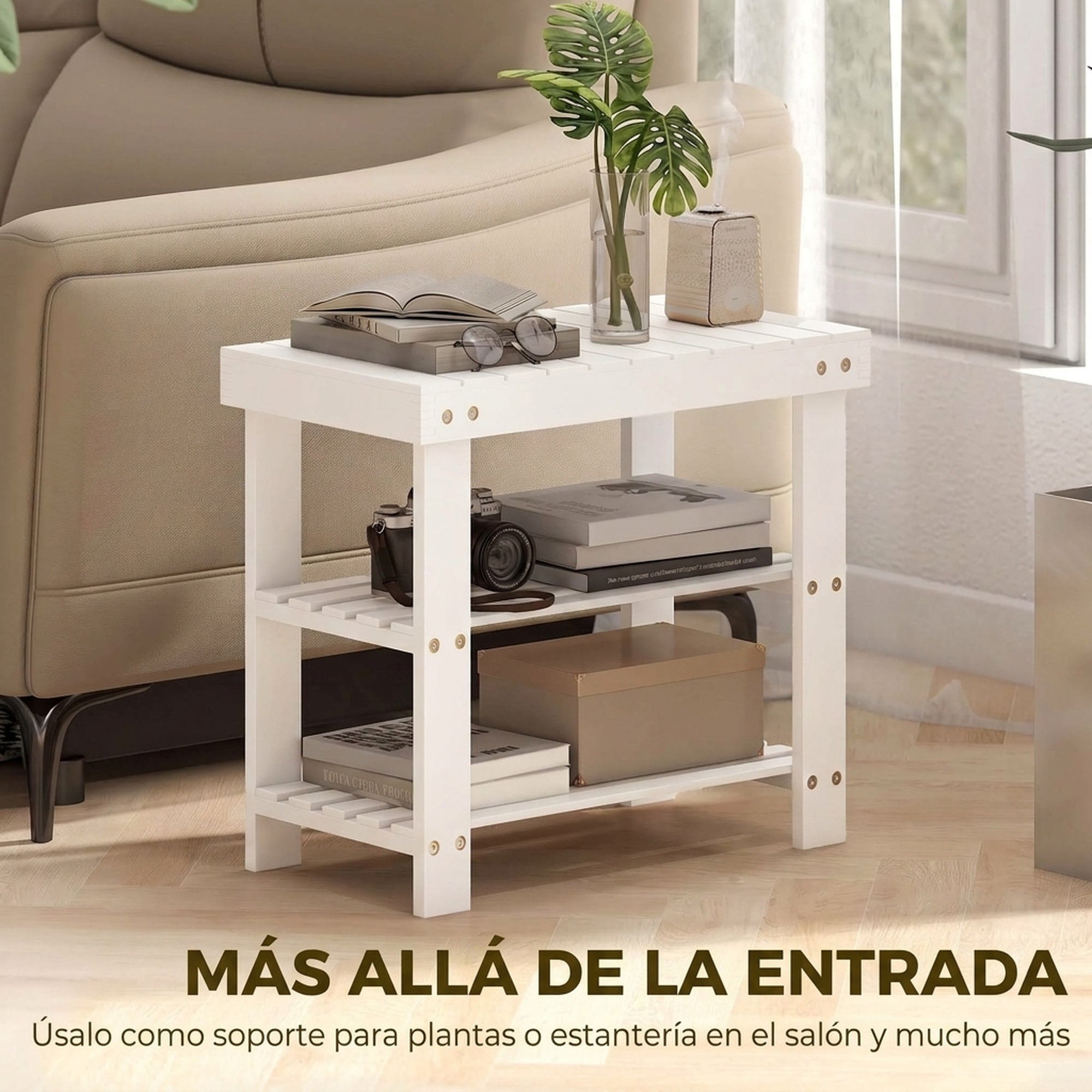 Una mesa auxiliar de madera blanca con libros, una cámara y una planta, situada junto a un sofá beige.
