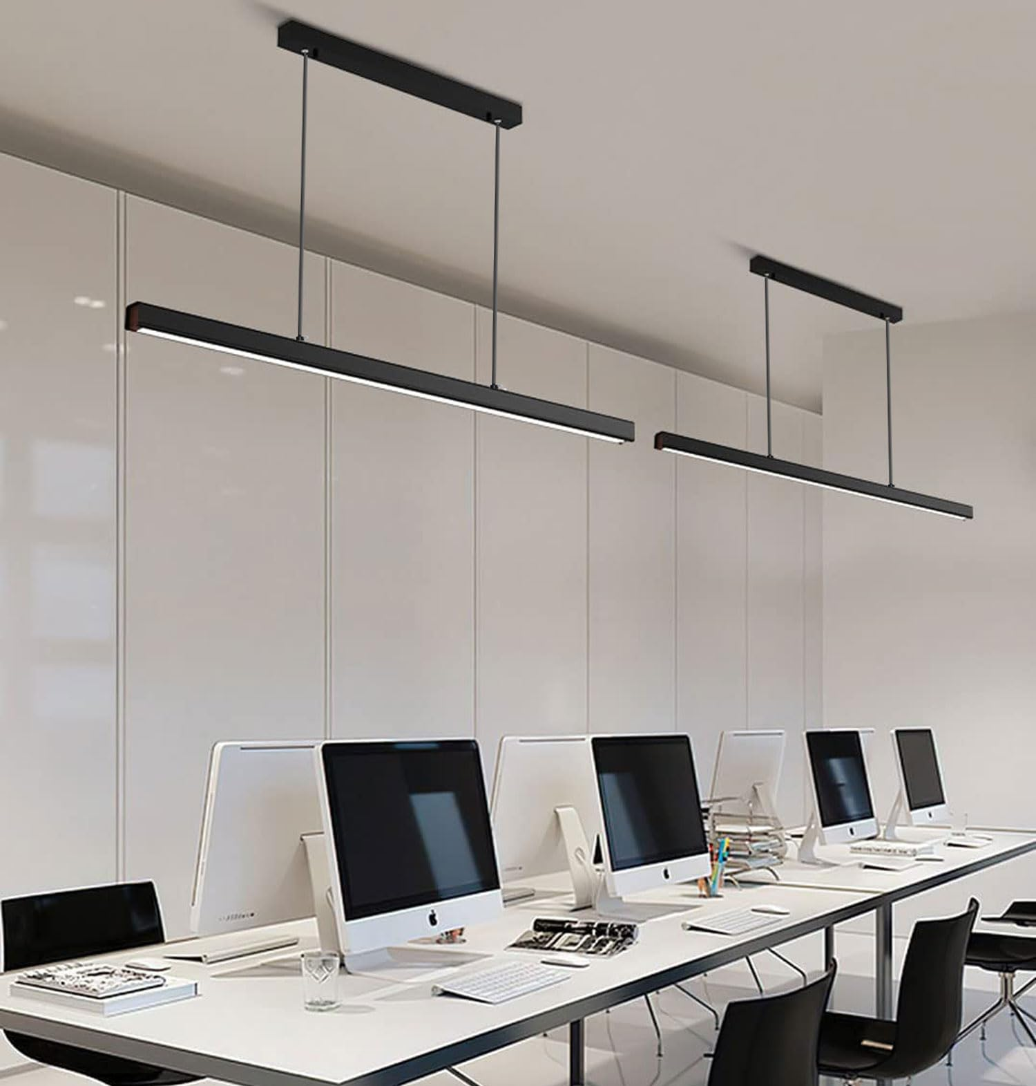 Moderne lange Pendelleuchten hängen über weißen Schreibtischen mit Computern in einem hellen Büro.