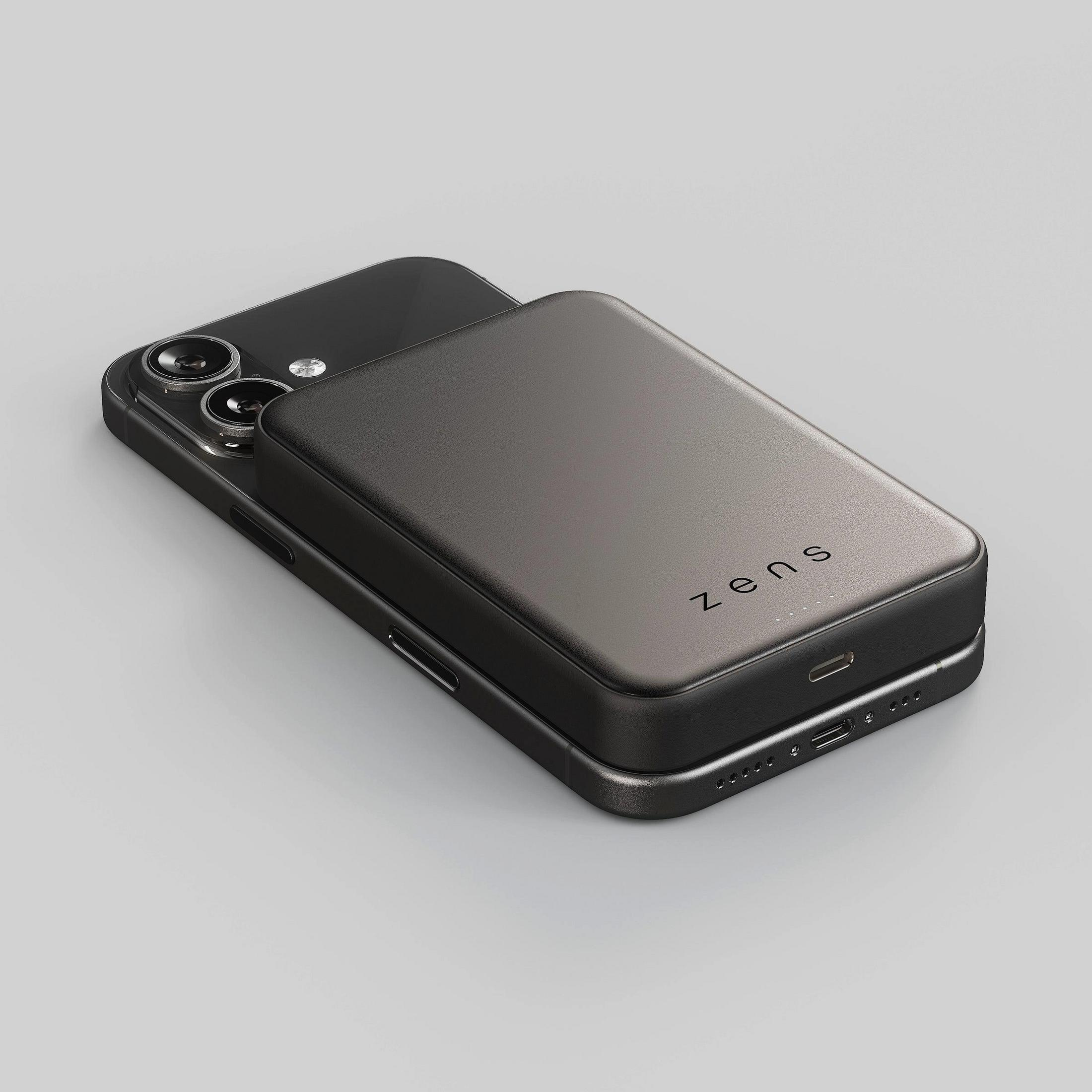 A black smartphone with a magnetic Zens power bank attached to its back on a light background.