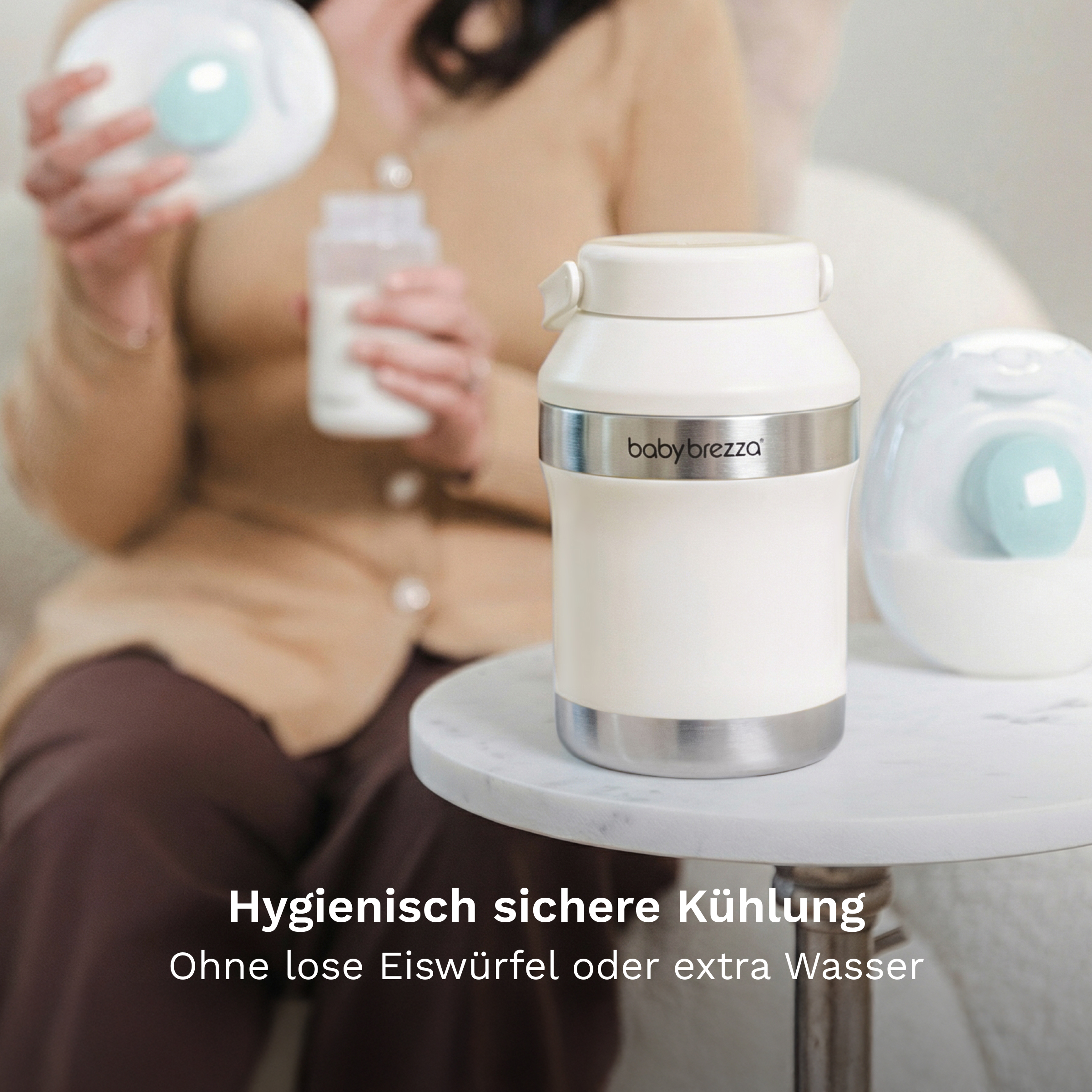 Ein weißer Baby Brezza-Kühler steht auf einem Tisch, im Hintergrund hält eine Frau Milchflaschen.