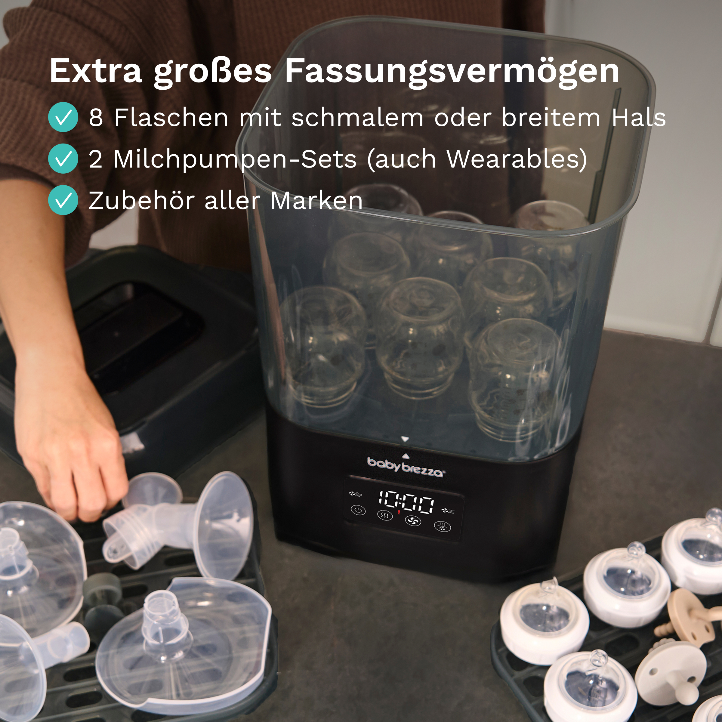 Ein Baby Brezza Sterilisator gefüllt mit Flaschen, umgeben von Pumpteilen und deutschem Text.