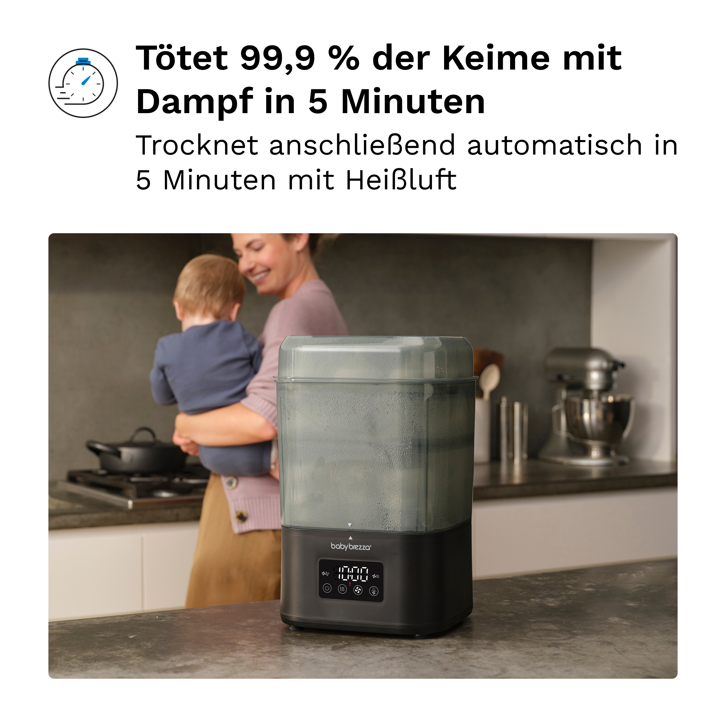 Ein Babybrezza Dampfsterilisator auf einer Küchenarbeitsplatte, im Hintergrund hält eine Mutter ihr Baby.