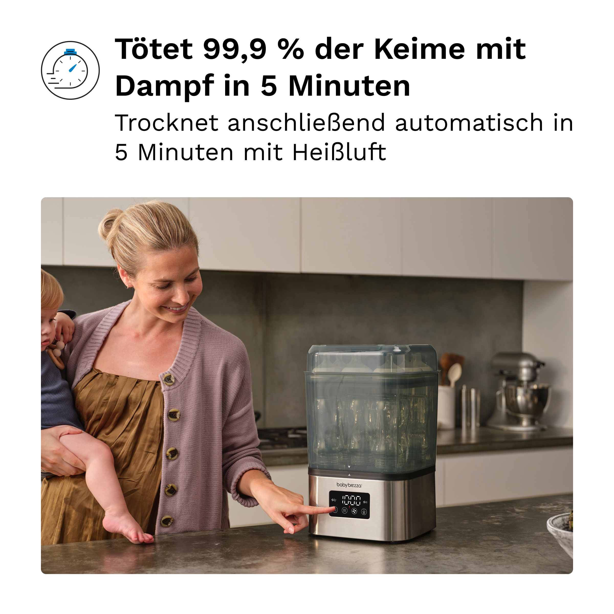 Eine Frau hält ein Baby und bedient einen Babybrezza-Flaschensterilisator in einer Küche.