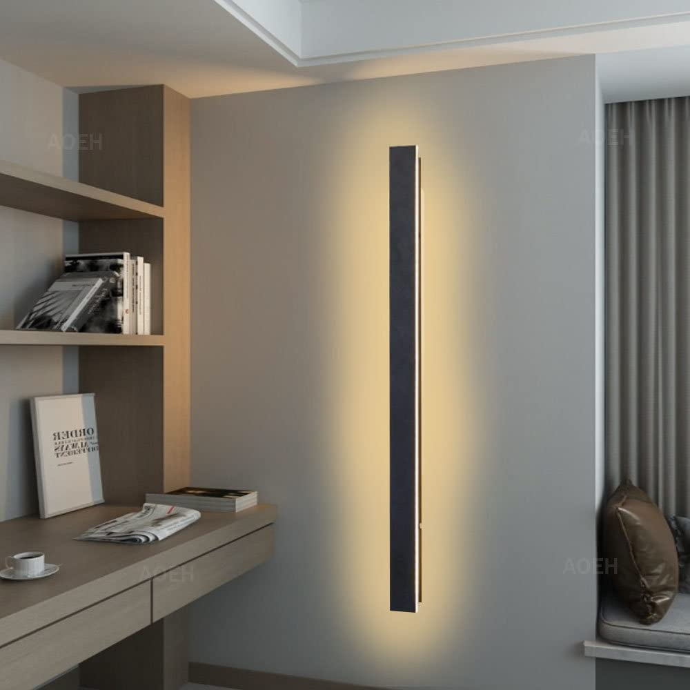 Eine lange, vertikale Wandleuchte strahlt sanftes gelbes Licht an einer grauen Wand in einem modernen Zimmer aus.