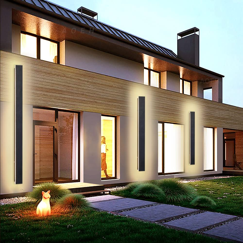 Moderne Hausfassade in der Dämmerung, beleuchtet durch lange Wandleuchten und eine leuchtende Katzenlampe.