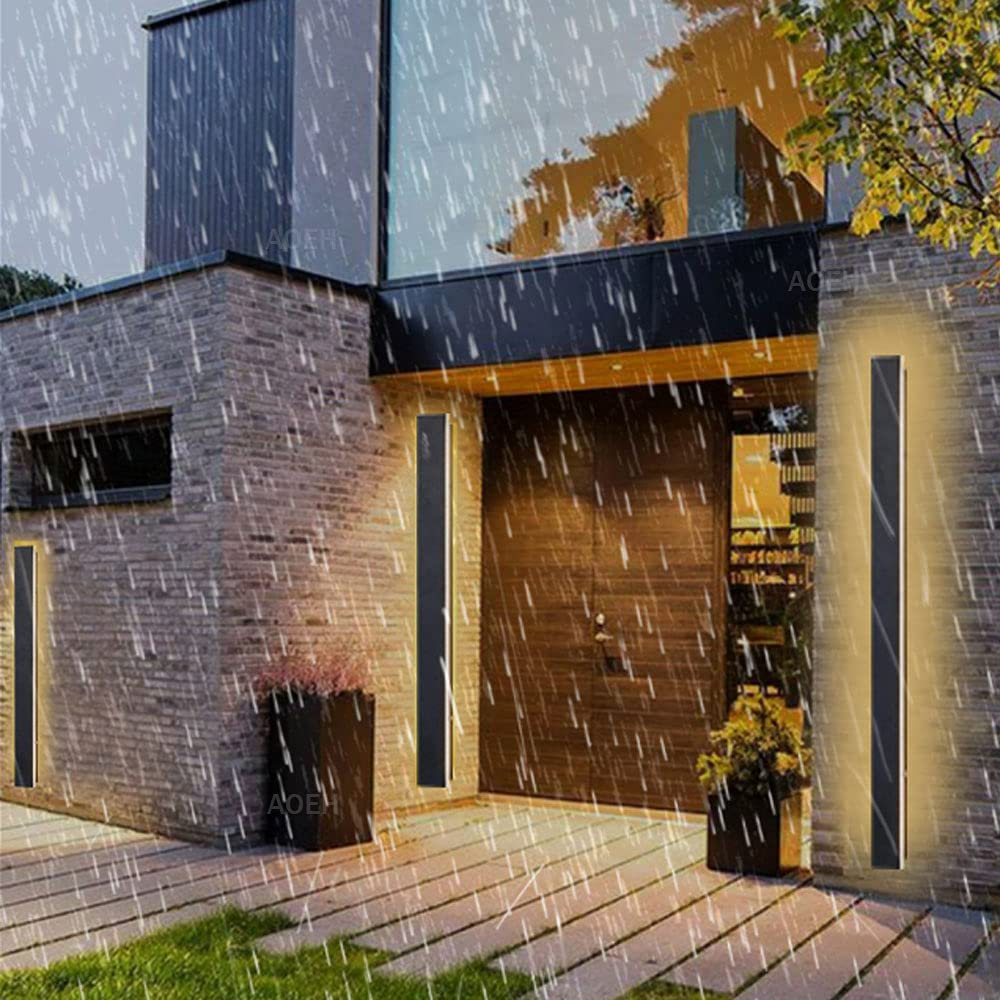 Moderne Ziegelhausfront im Regen mit beleuchteten Wandleuchten neben der Eingangstür.