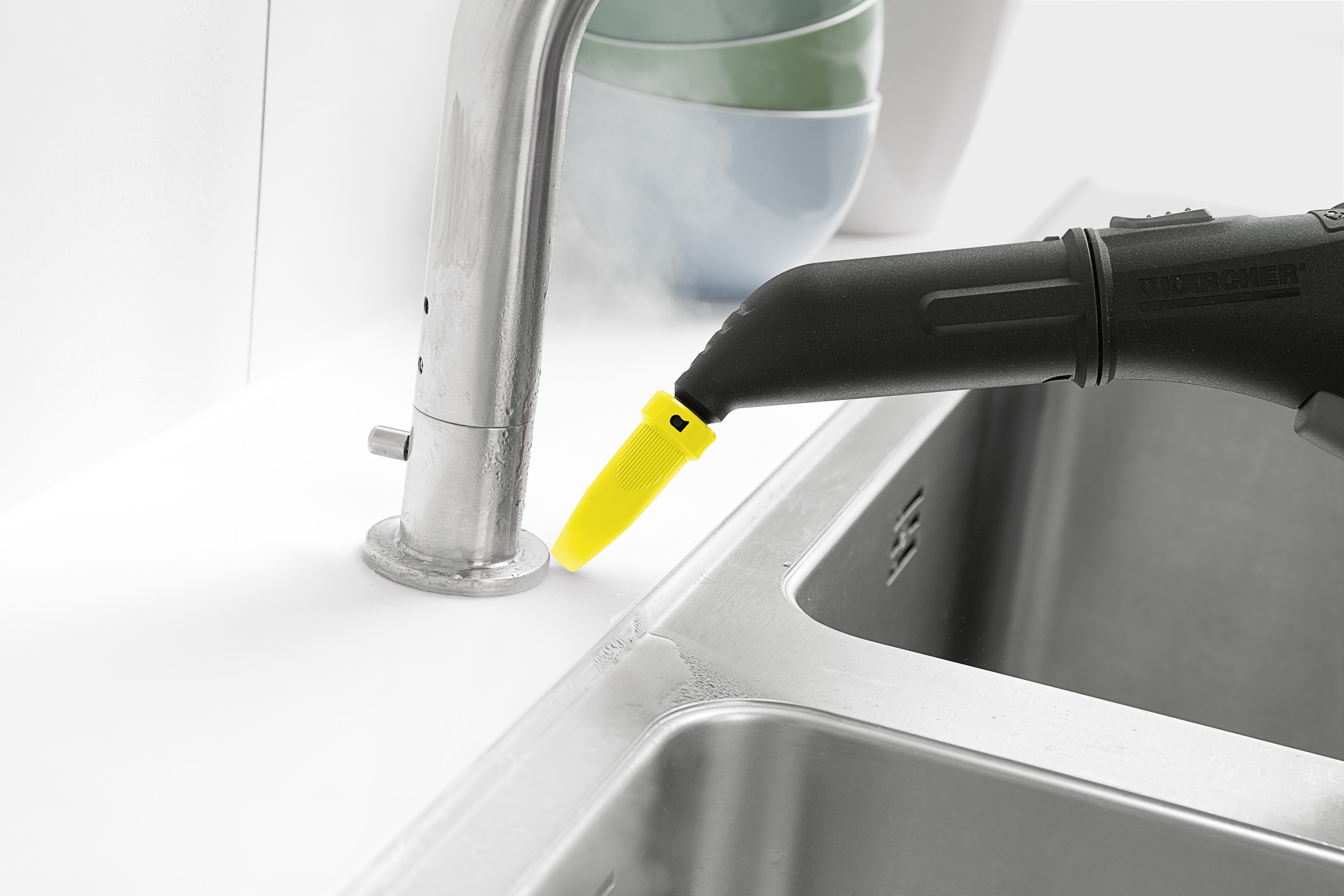 Eine schwarz-gelbe Dampfreinigerdüse sprüht Dampf auf einen Küchenarmatur neben einer Edelstahlspüle.