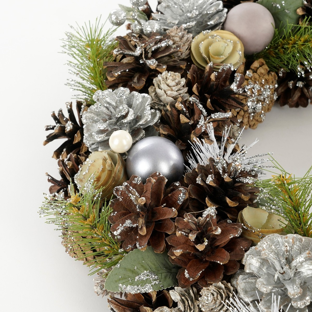 Weihnachtskranz mit Tannenzapfen, Silberkugeln, grünem Laub und künstlichem Schnee.