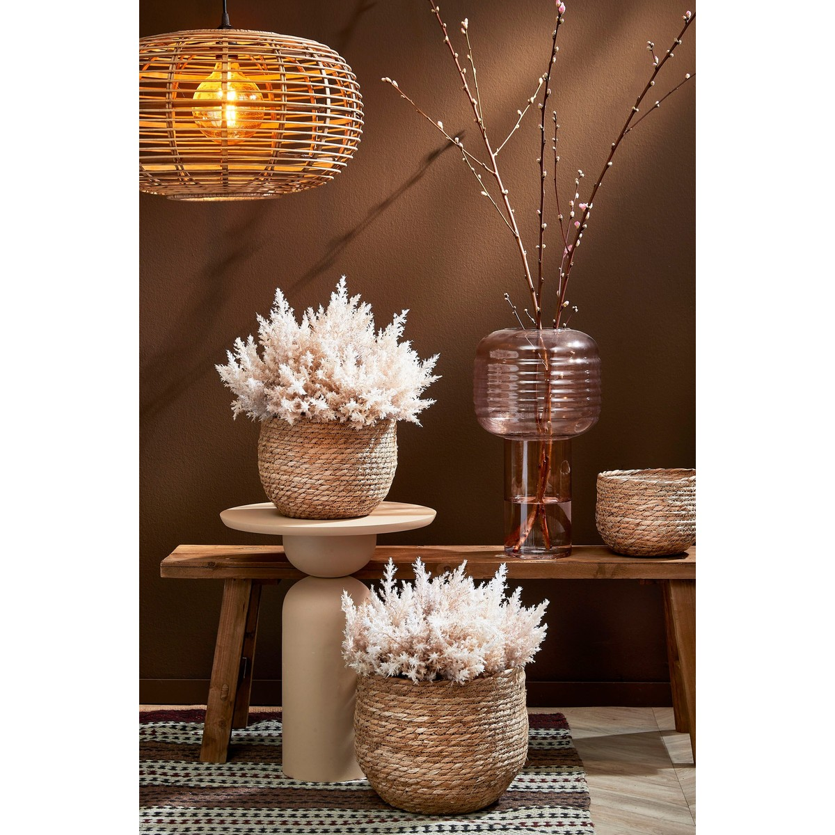 Wohnzimmer mit Rattanschirmlampe, Holzsitzbank und dekorativen Korbvasen vor brauner Wand.