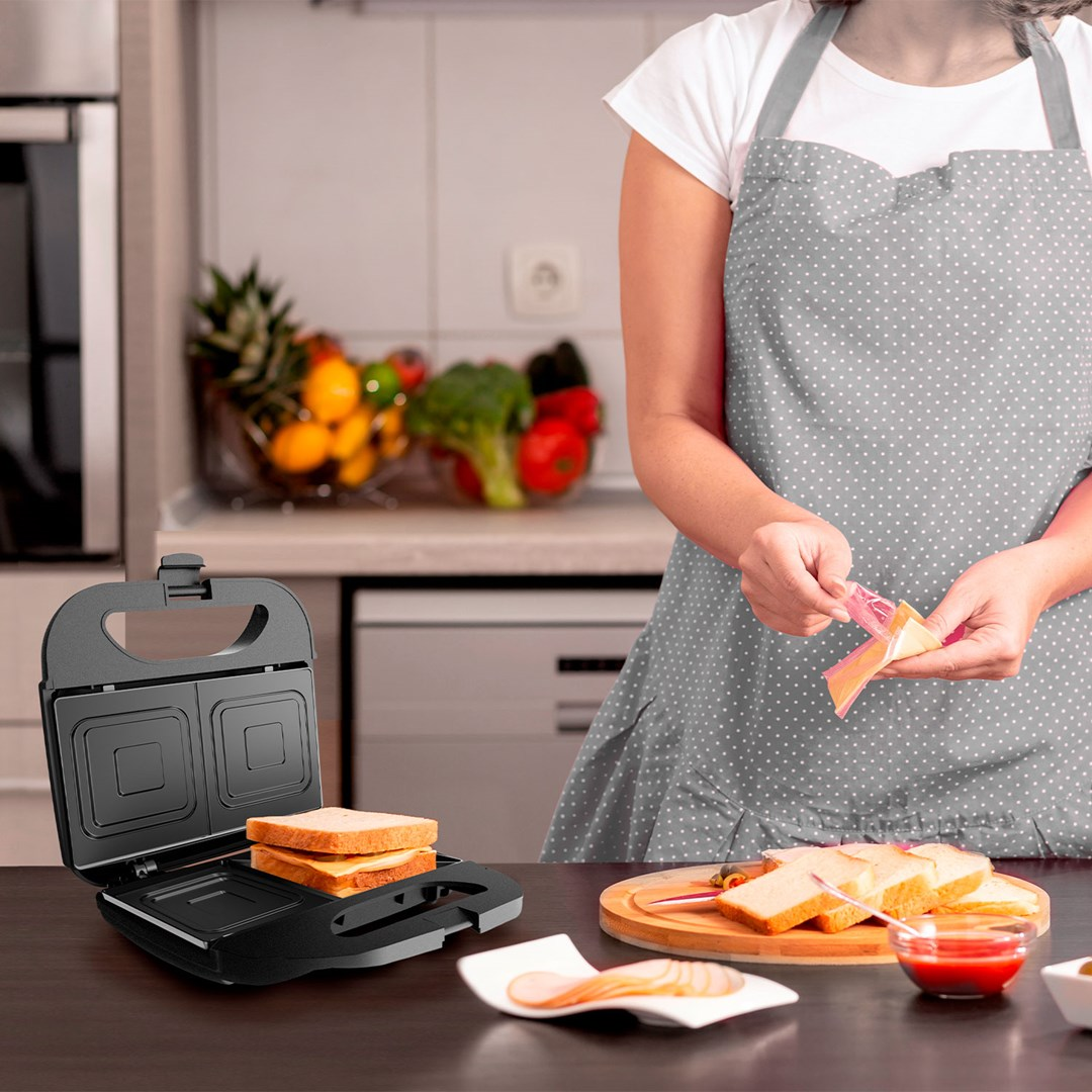 Eine Frau mit grauer Schürze bereitet Sandwiches in einer Küche zu.