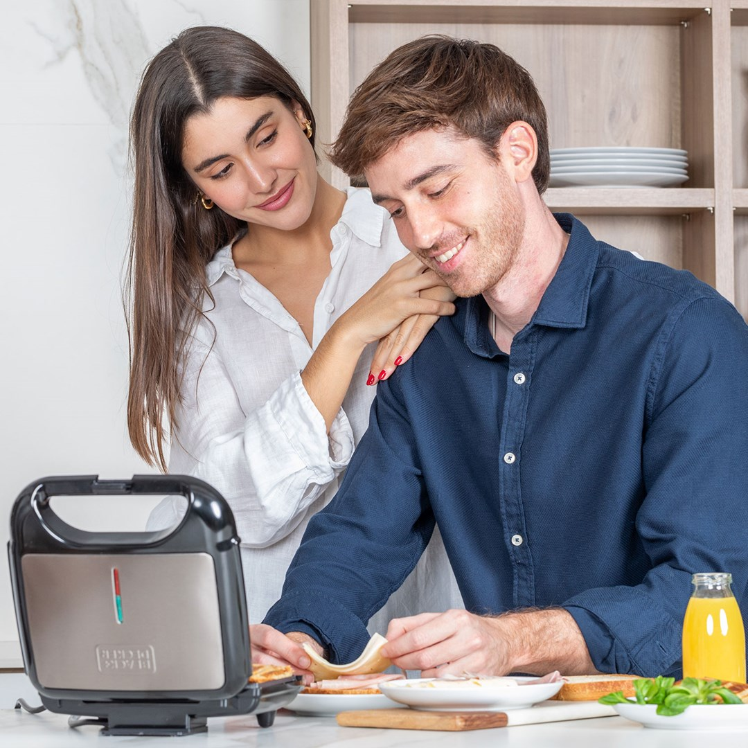 Ein Paar in einer Küche bereitet Sandwiches vor, neben einem Sandwichmaker.