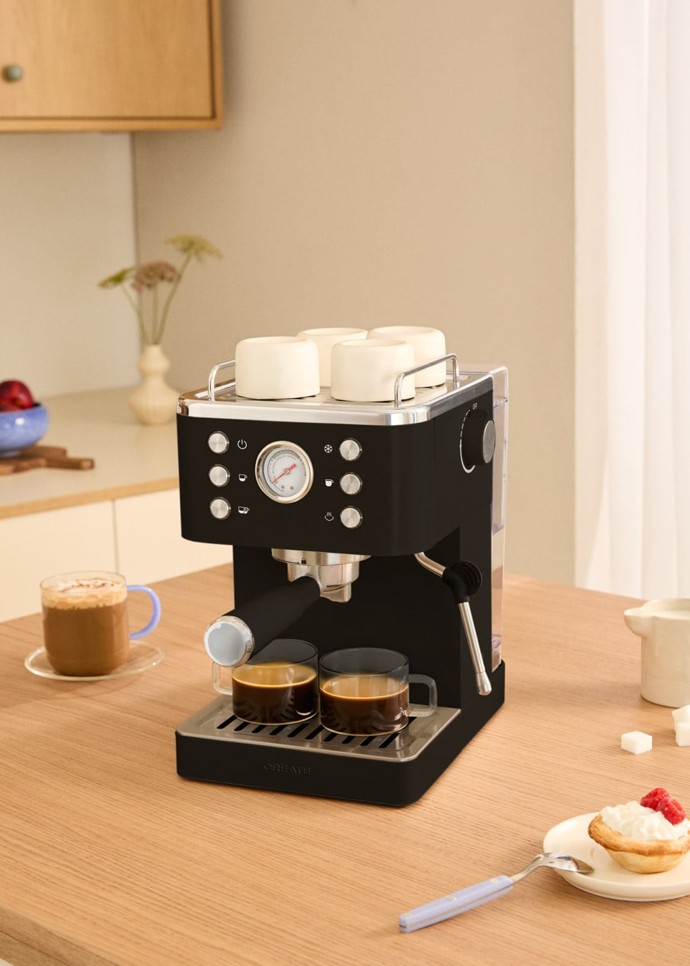Cafetera negra en mesa de madera con cuatro tazas blancas arriba y dos vasos de café abajo.