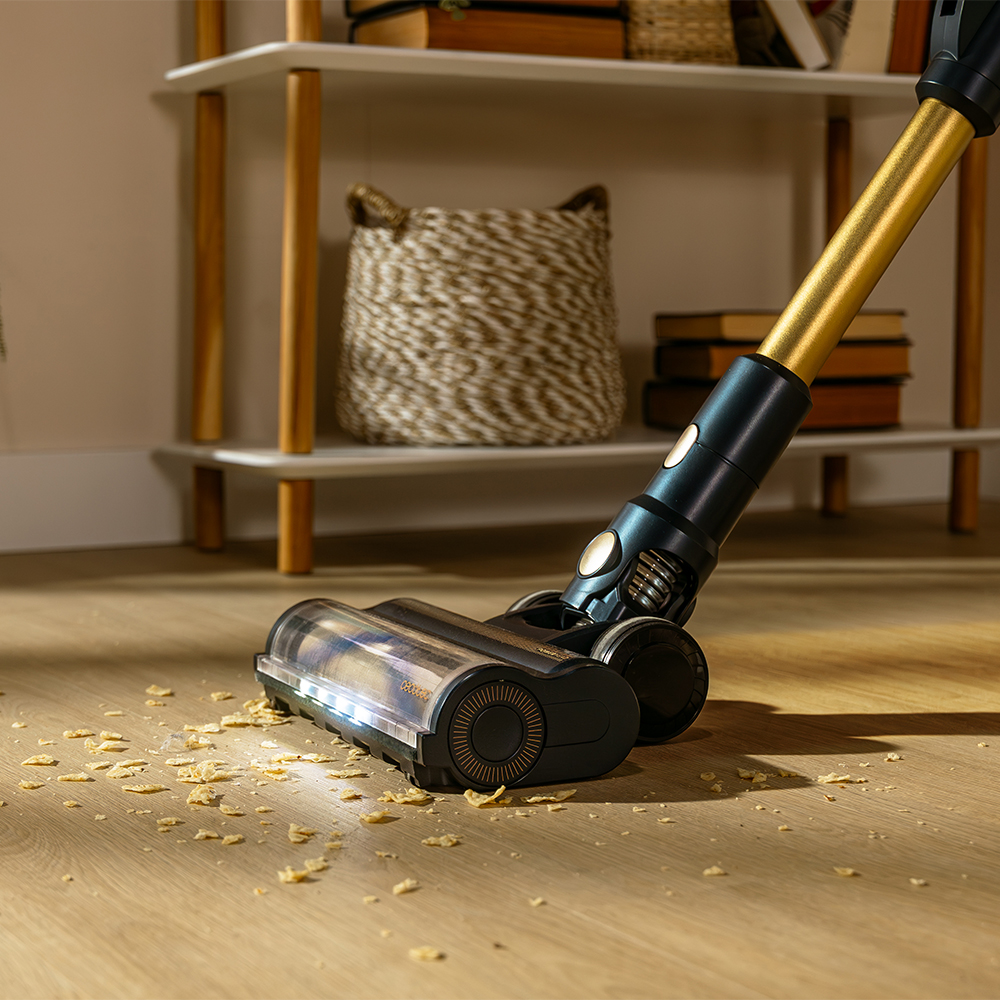 Una aspiradora sin cable aspira migas de comida de un suelo de madera en una habitación.
